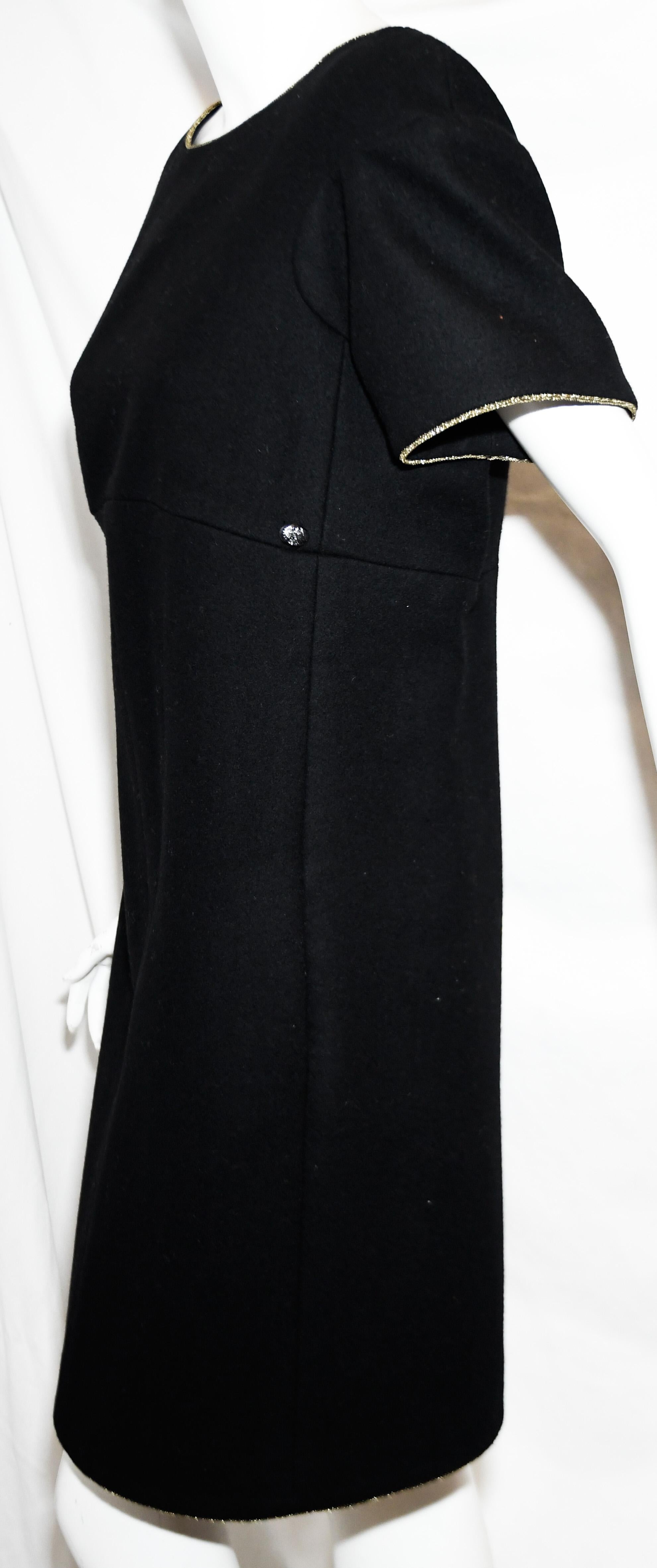 Chanel black wool A line dress is trimmed with gold tone cord around neckline and sleeve.   Dress has 3 plaquettes accentuating the front  of the dress and at one side CC Chanel button for decoration.  This dress is lined in black Camellia silk