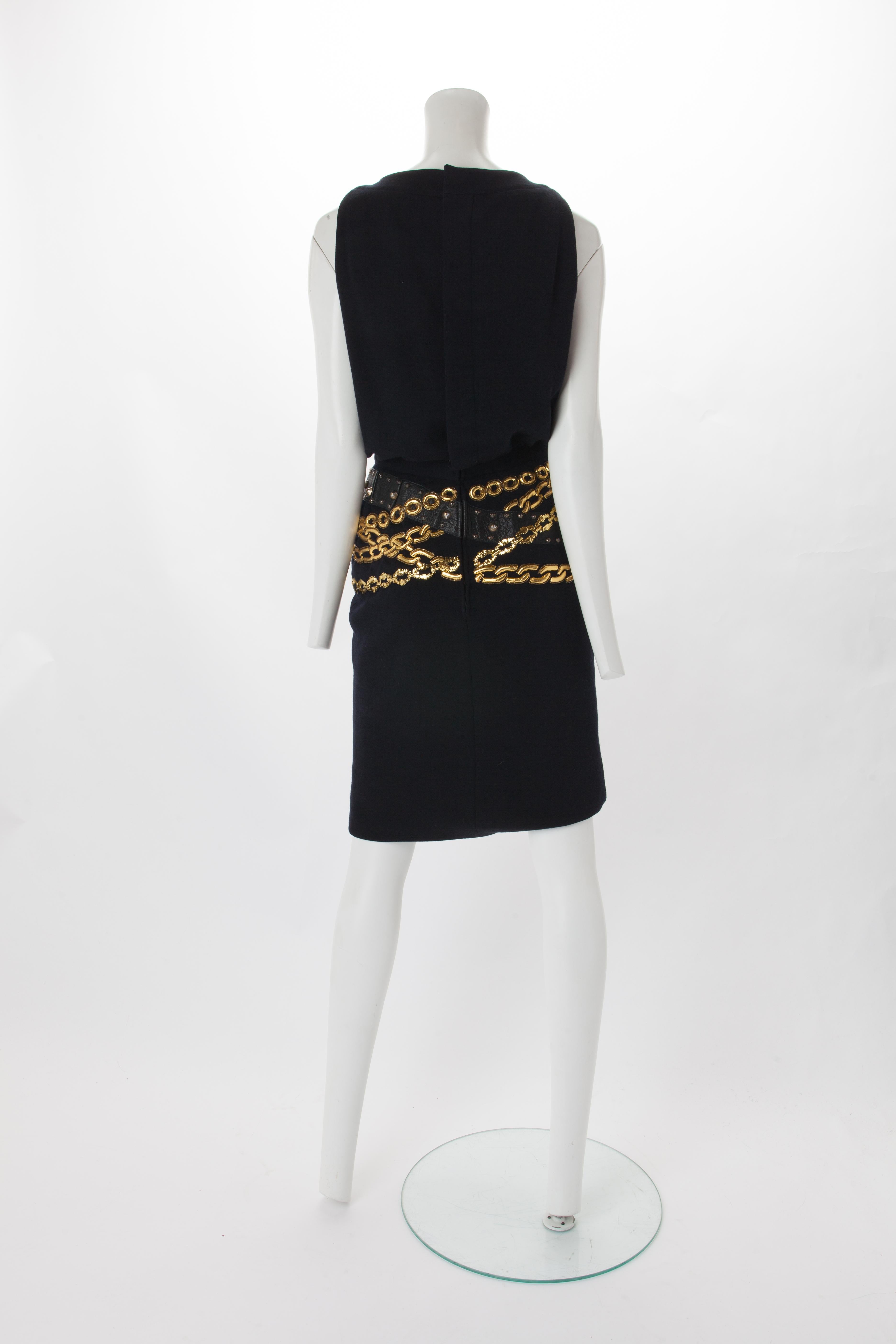 Chanel Black Wool Dress with Gold Chain Trompe L'oeil, 1985.
Crew neck wool dress with buttons down the center of the bodice and two buttoned pockets at bust. Features waist band with black leather and gold chain detail wrapping around the hip.