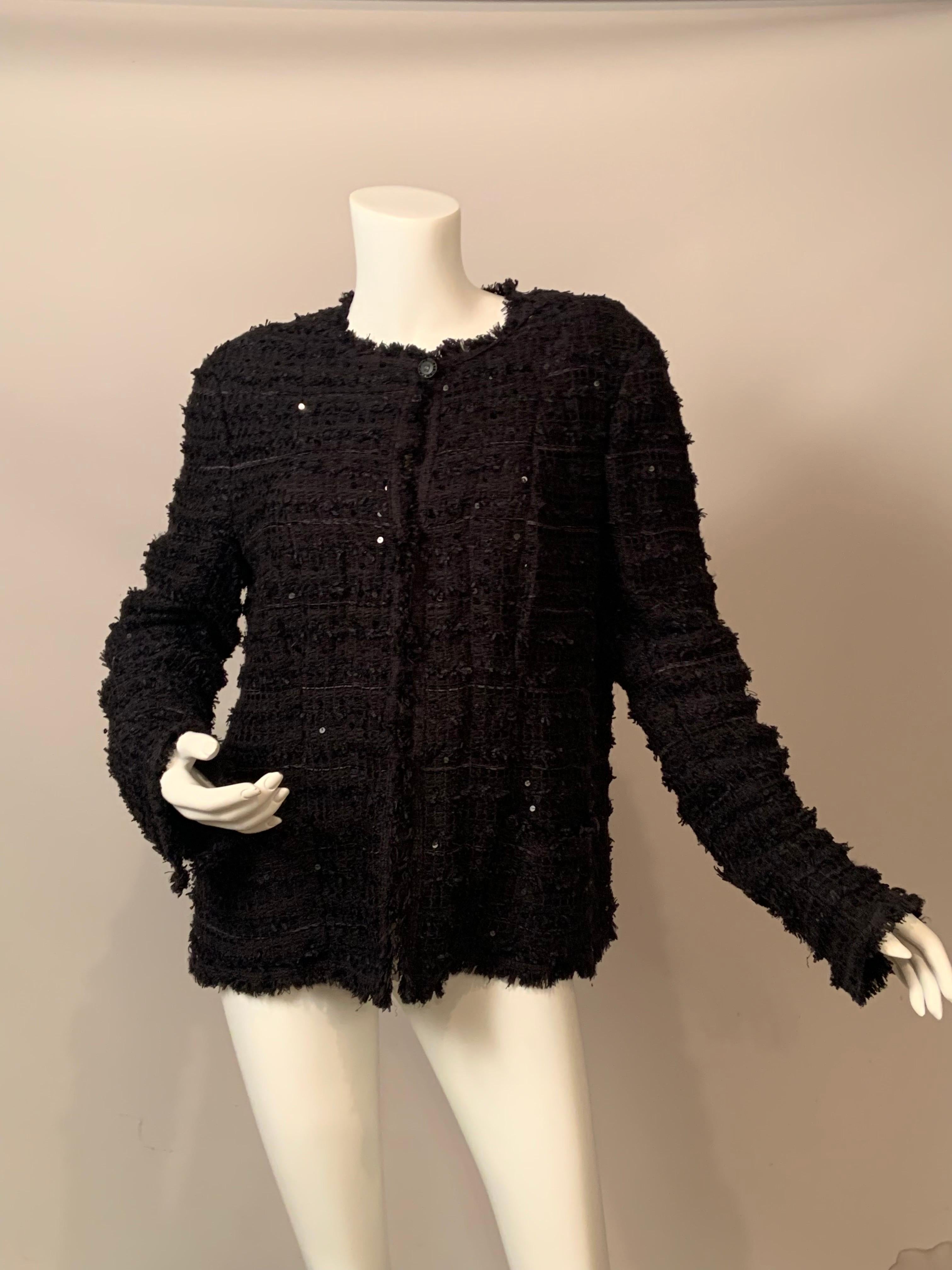 Una classica giacca in stile Chanel, disegnata da Karl Lagerfeld, diventa molto moderna con l'aggiunta di paillettes nere e di un sottile nastro di seta intrecciato nel tessuto di lana nera di questo elegante capo da sera.  A prima vista, le