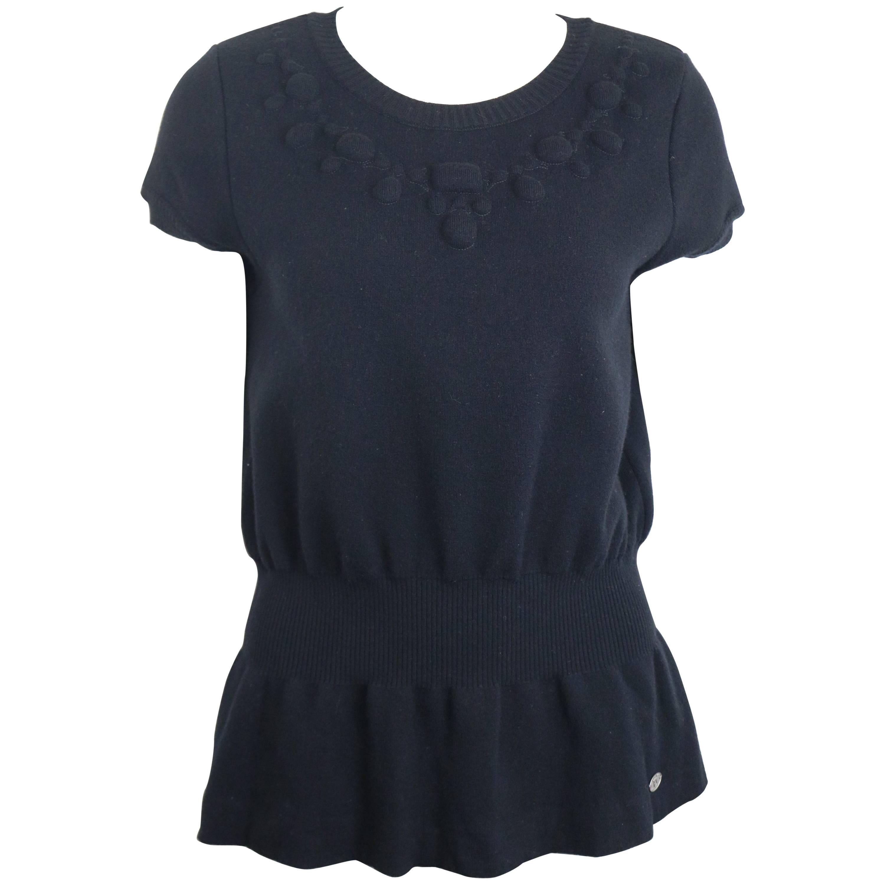 - Top a maniche corte in lana nera di Chanel della collezione A/I 2007. 

- Dettagli decorativi. 

- Girovita e maniche a coste. 

- Effetto pieghettato sul fondo.

- Taglia 44. 

- 100% Lana. 