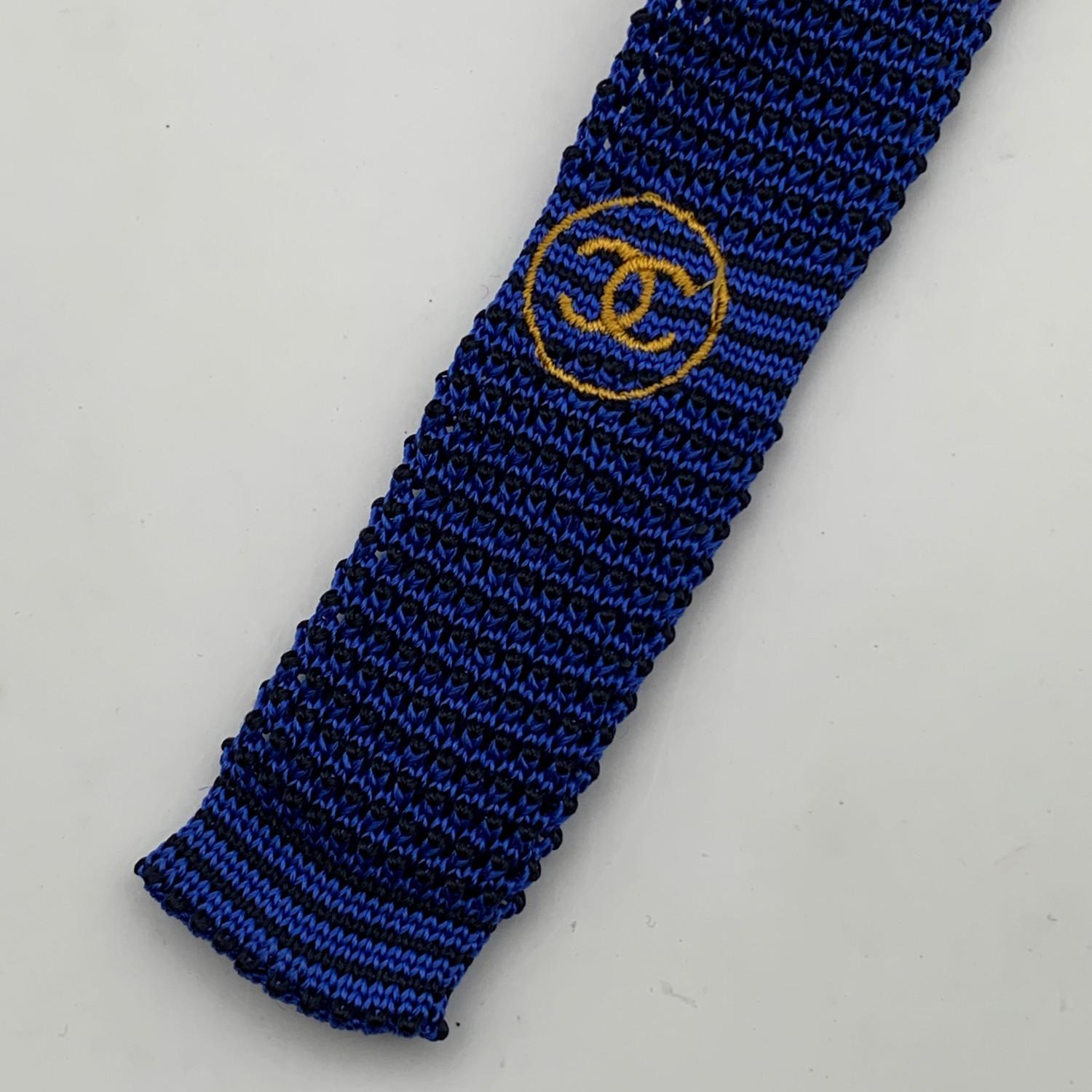 Elegant Chanel knitted neck tie in blue and black color. Gold metal chain detail on the back along the hem. Embroidered CC Logo in yellow color. Scalloped hem. Composition: 100% Silk. Chanel composition tag attached. Made in Italy. Total length: 57