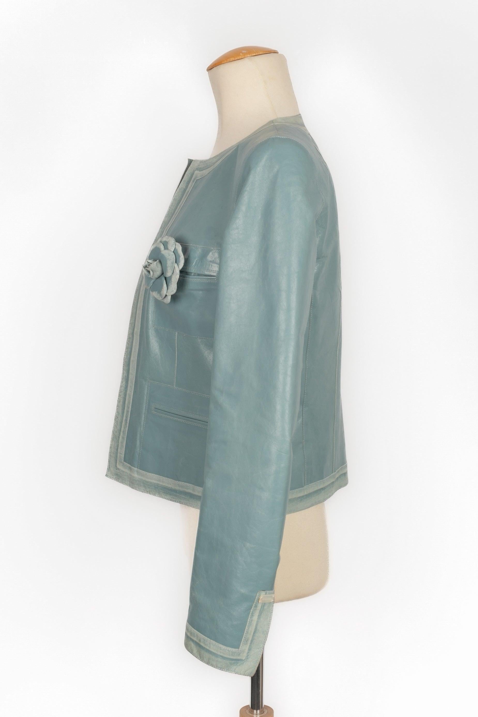 Chanel - (Made in France) Blue calfskin jacket decorated with a camellia brooch. Silk lining. Size 36FR indicated. 2003 Spring-Summer Collection, under the artistic direction of Karl Lagerfeld. Very good general condition, but there are some tiny
