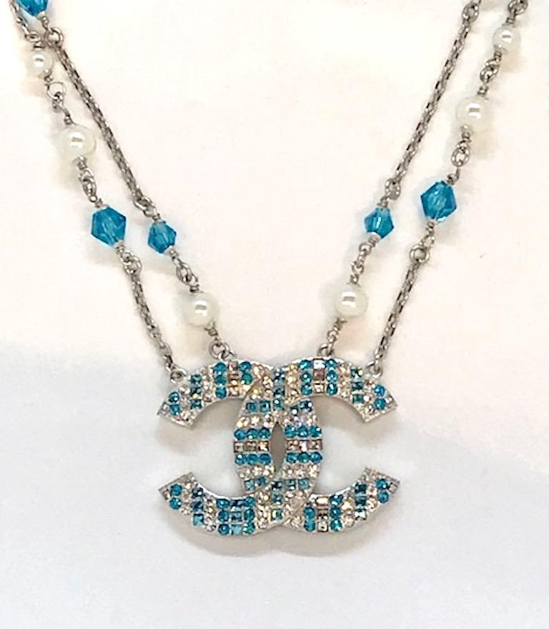 A lovely Chanel double strand interlocking necklace with a large central Chanel CC logo pendant. Silver tone chain and pendant with sky blue faceted crystal and pearl beads. The interlocking CC logo is encrusted with round and square clear and