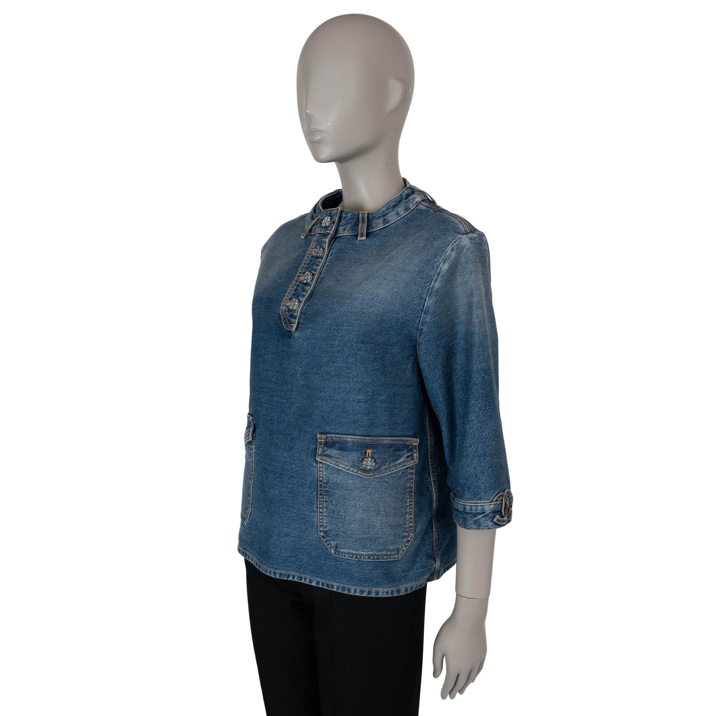 This 100% authentic Chanel blouse in blue washed denim cotton (100%) blends casual elegance with signature detailing. Designed with a relaxed silhouette, it features a round neck with belt loops, 3/4 sleeves adorned with CC patches at the cuffs, and