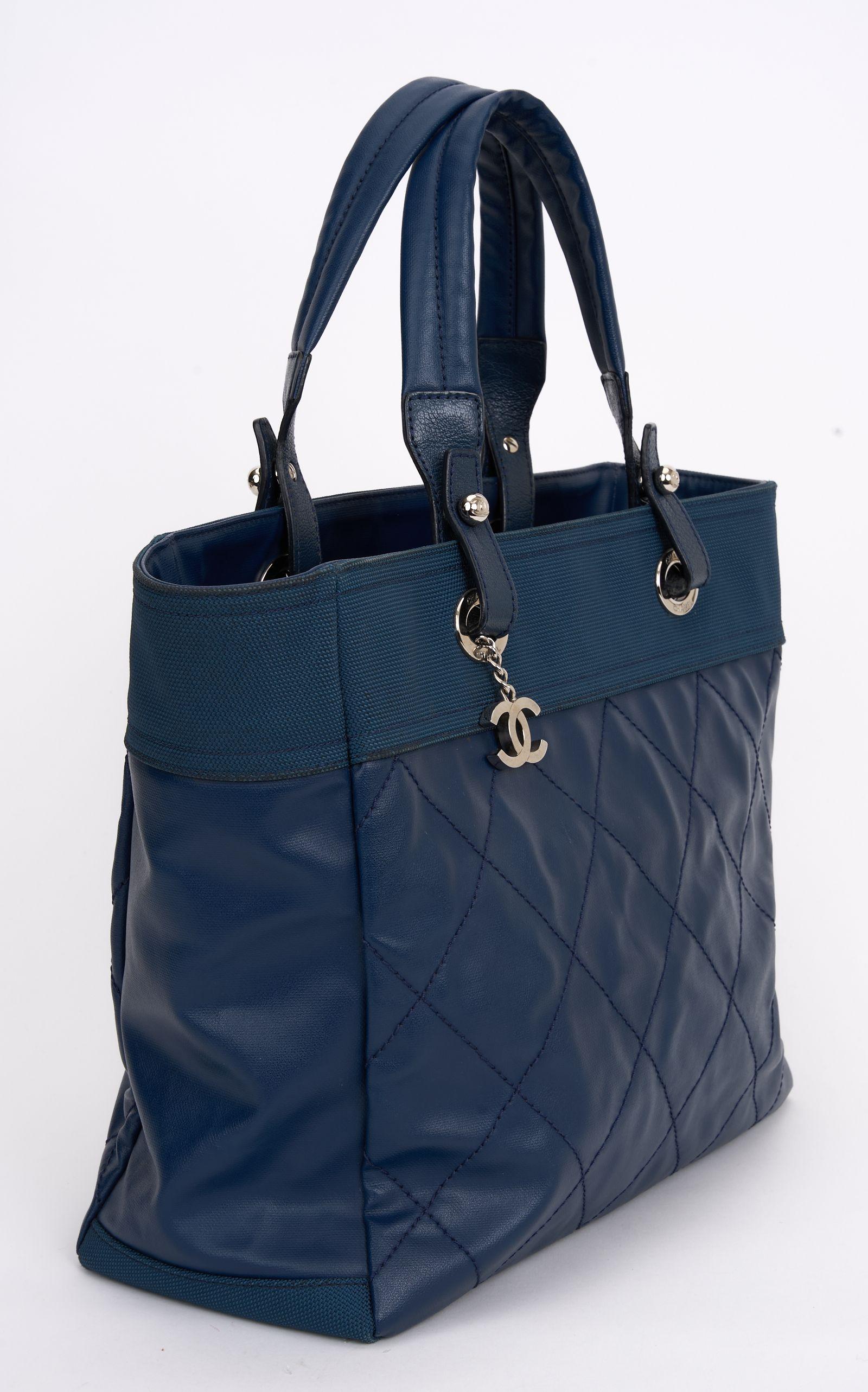 Questa Chanel Paris-Biarritz PM Tote è realizzata in tela blu e pelle trapuntata a rombi, con due manici superiori, charms con logo CC e finiture in argento. La parte superiore ha una chiusura a zip e si apre con una fodera in tela blu, una tasca