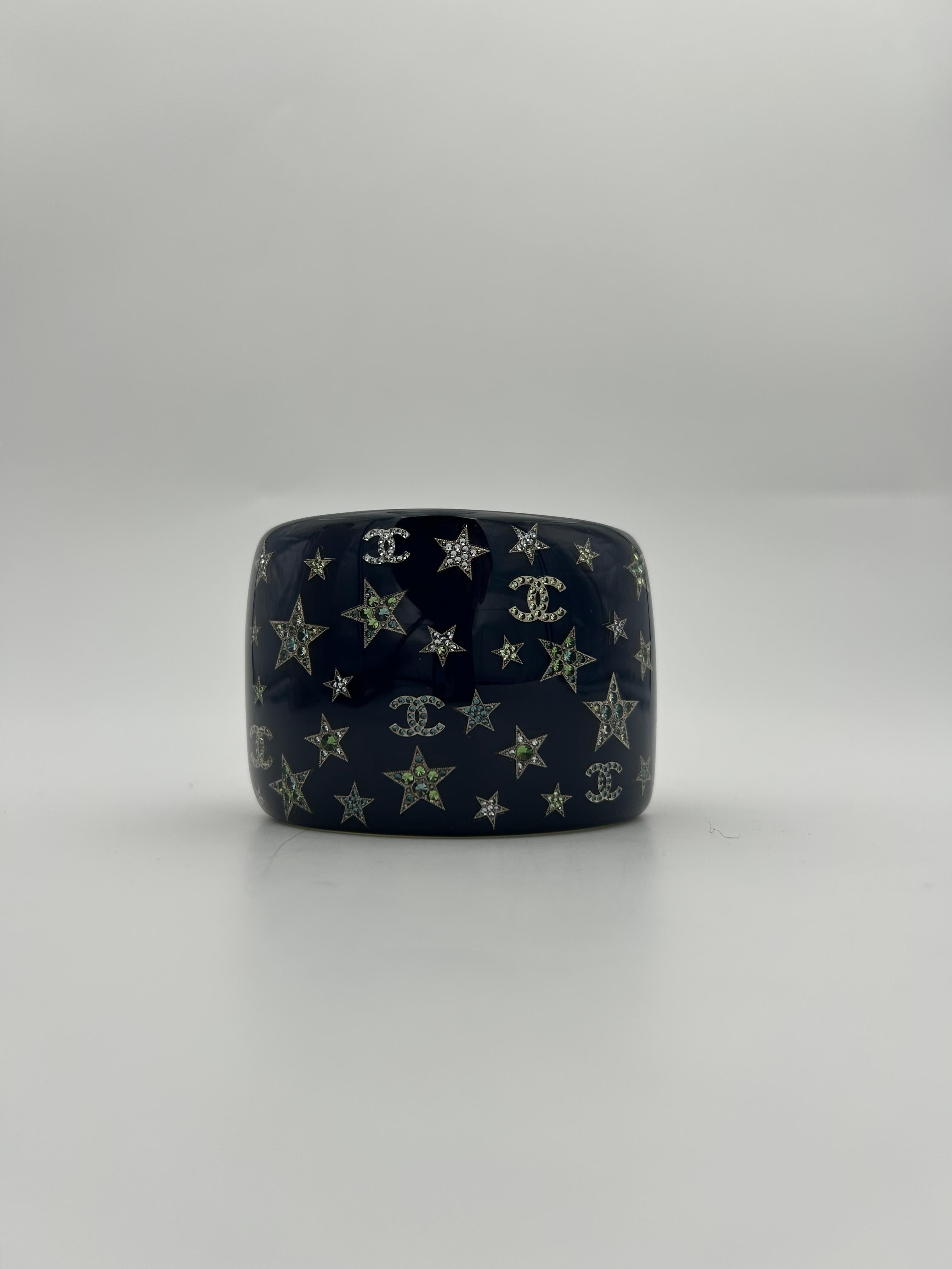 Chanel Bracelet manchette CC et étoile en strass bleu 2012. Collection S/Summer 2012 en bon état. Ce bracelet présente le logo CC et les étoiles emblématiques de Chanel, ornés de cristaux étoilés sertis sur un fond de résine bleu nuit. Ce site  cuff