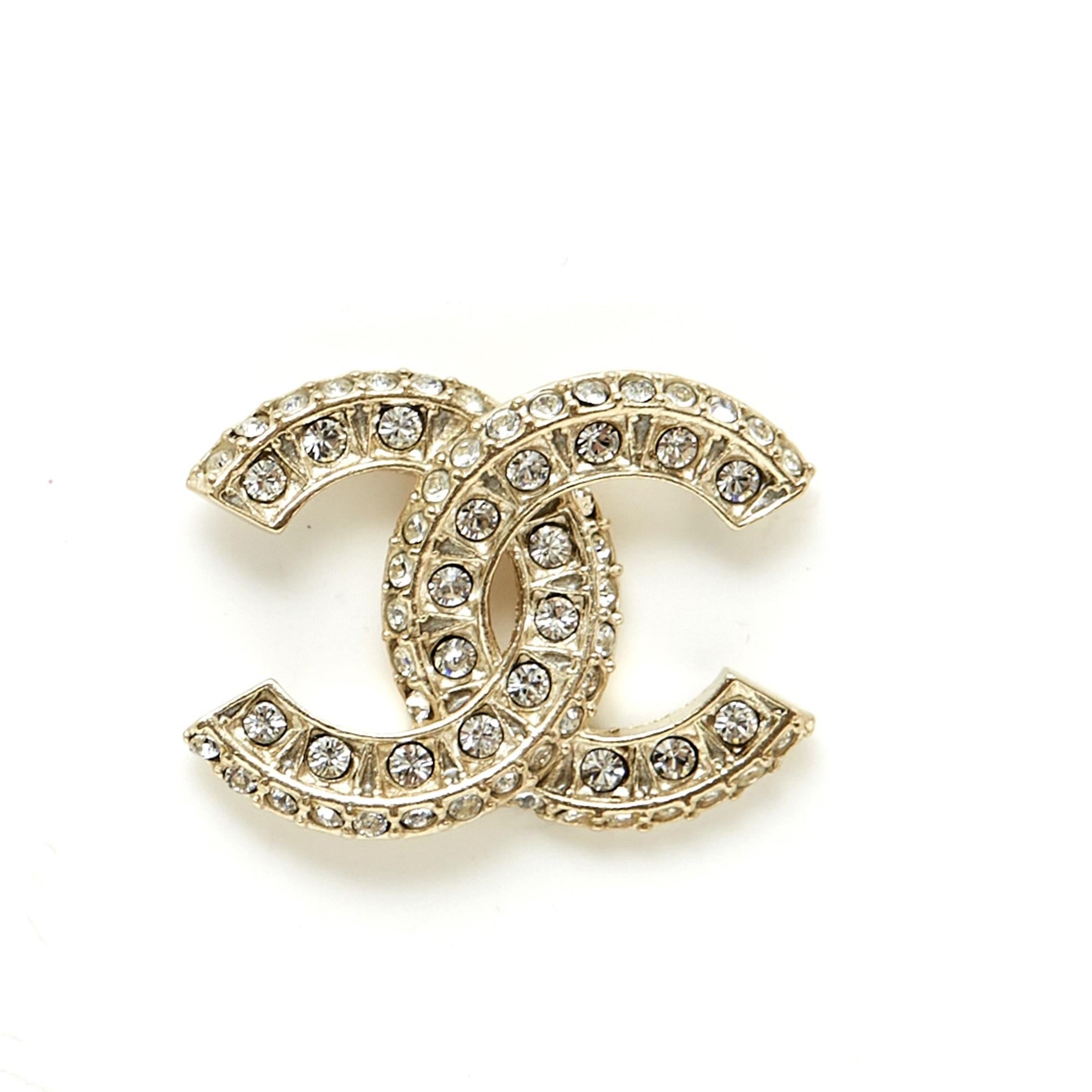 Boucles d'oreilles en métal légèrement doré (entre l'or et l'argent) façonnées et incrustées de 2 rangées de strass blancs. Largeur 2 cm x hauteur 1,45 cm. Les boucles d'oreilles sont livrées sans facture ni emballage d'origine, elles sont