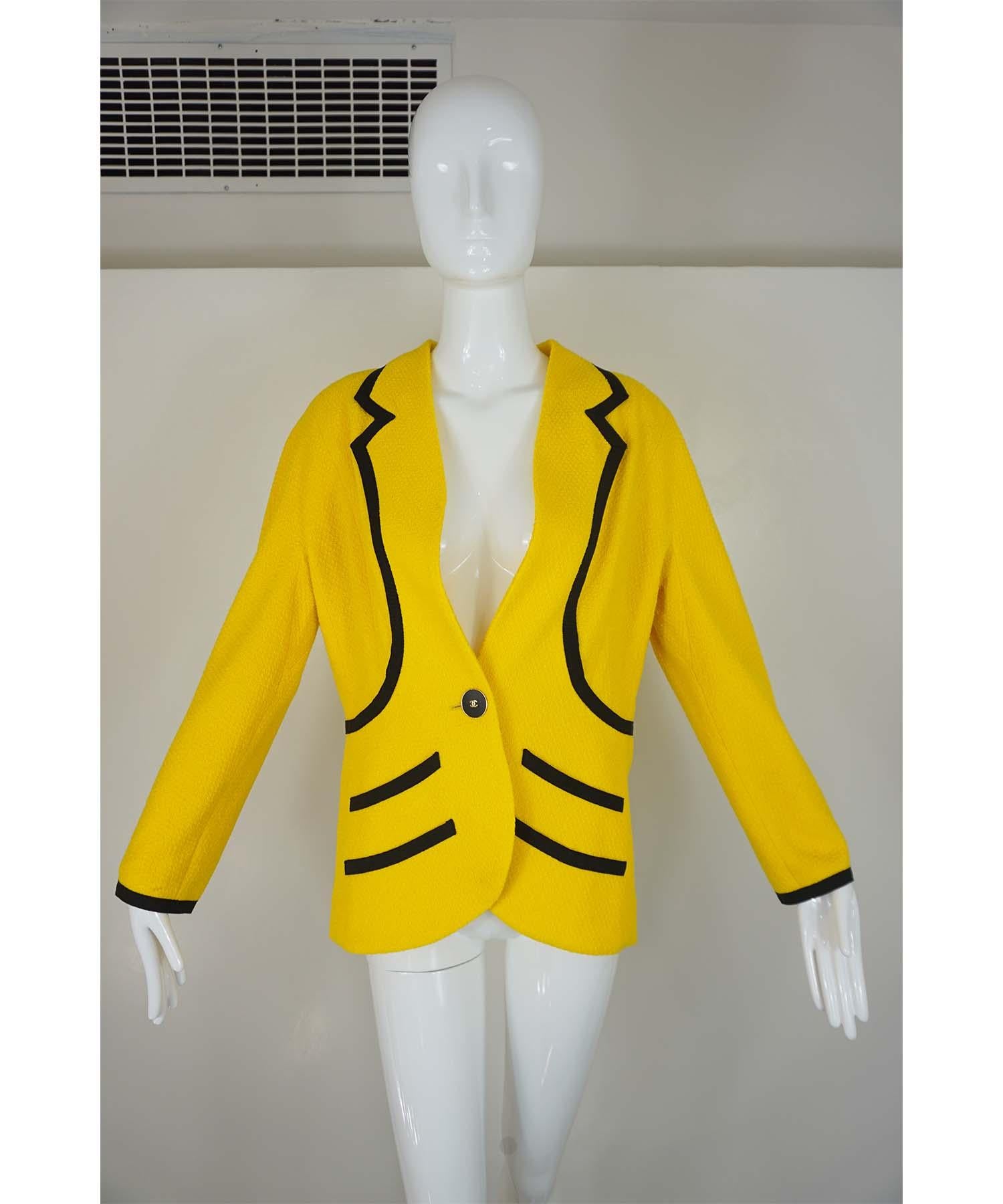 Chanel Boutique vintage jacket, from their 1993 Cruise Collection,  is featured in yellow wool with black ribbon trim and four front mock pockets.  The jacket is adorned with large black and gold CC button closure and three matching smaller black