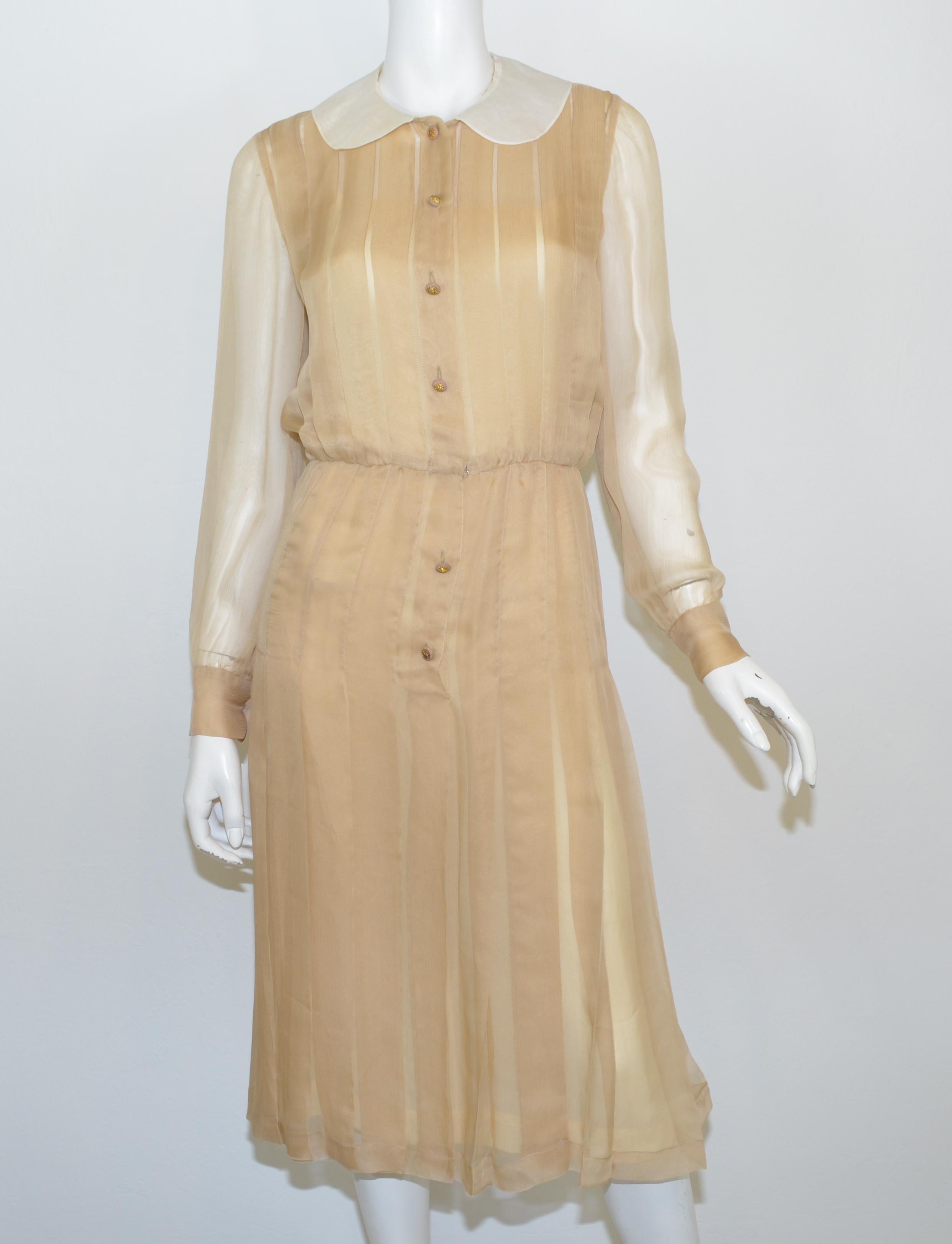 Chanel Boutique dress is featured in a beige-colored silk chiffon fabric with a pleated design, a white Peter Pan organza collar, and gold-tone Lion head button closures that line down the front as well as on the cuffs. Dress includes a neutral slip