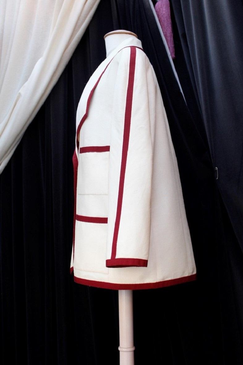 Chanel Boutique (Made in France) White silk jacket trimmed with a burgundy ribbon. It closes with a single button covered with burgundy fabric and decorated with a gilded metal cc logo. It is lined with a cream color silk. Indicated size