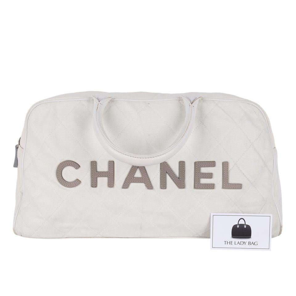 Authentic, pre-owned Chanel bowler bag with a white canvas and gray leather lettering. Features white and gray canvas, leather handles, leather lined interior with zipper pockets, rear zipper pocket, and silver hardware with gray CC zipper pull.