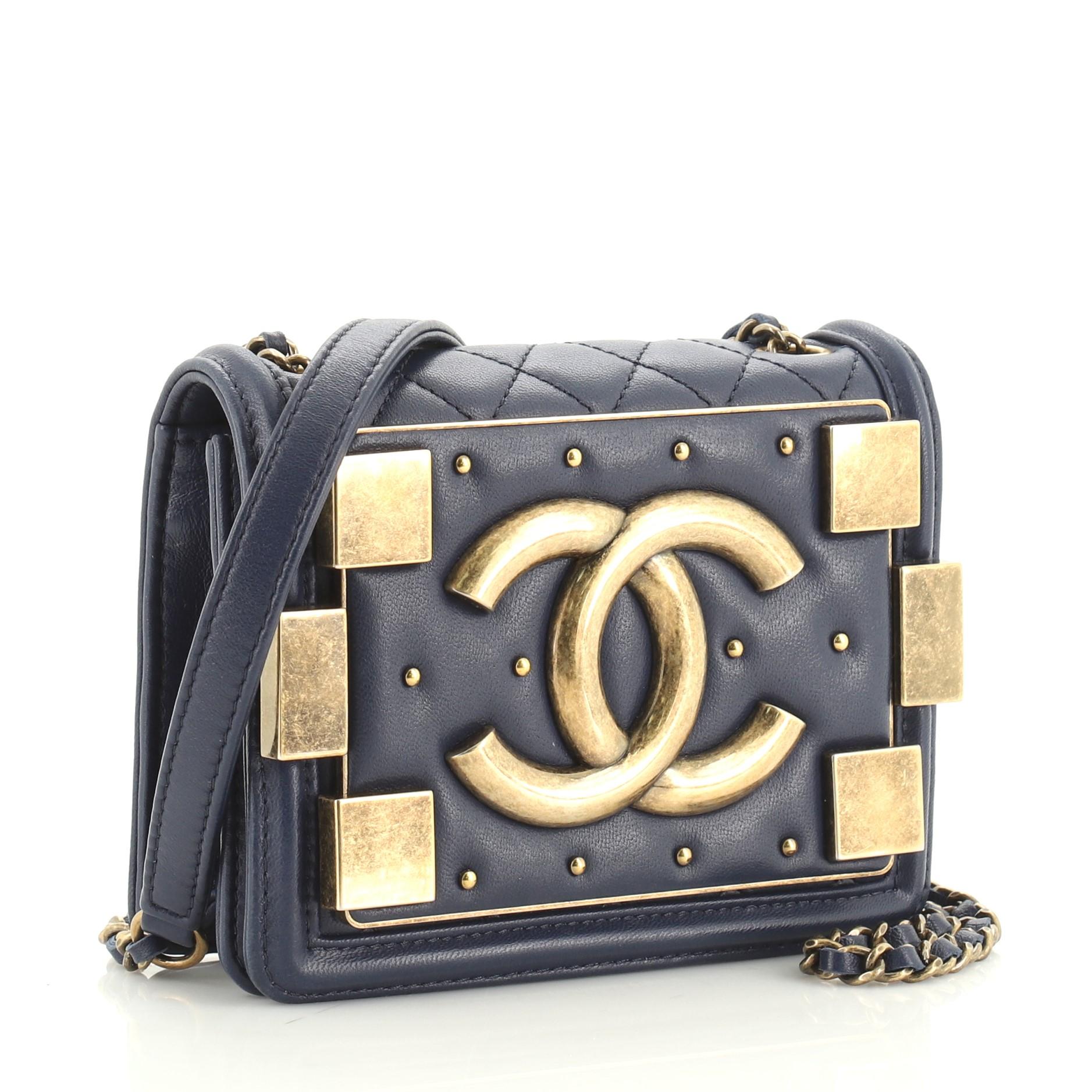 This Chanel Boy Brick Flap Bag Studded Quilted Lambskin Mini, crafted from blue quilted lambskin leather, features woven-in leather chain strap with leather pad, front flap with CC logo, stud and brick detailing, and aged gold-tone hardware. Its