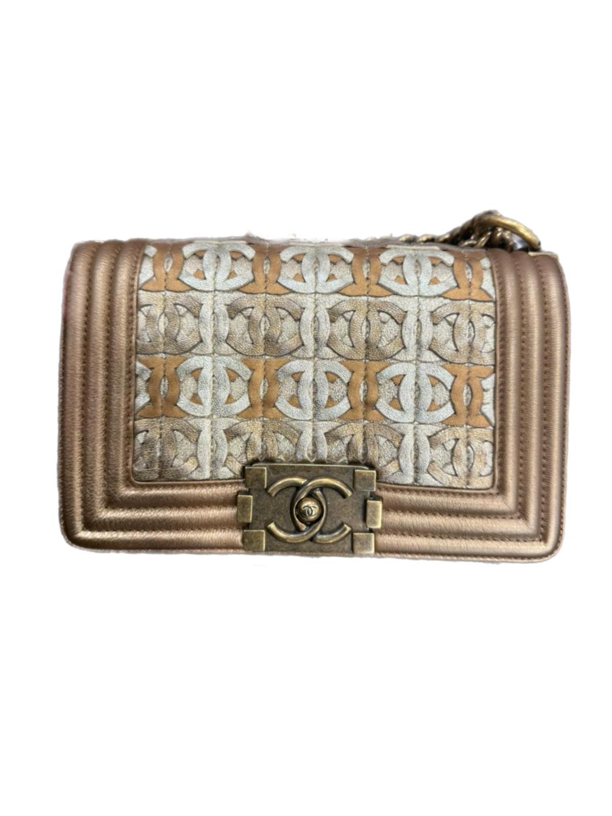 The Chanel Boy CC Logo Cut-Out Shoulder Bag in Metallic Gold is a striking statement piece that blends bold design with timeless luxury. Crafted from premium leather, its dazzling metallic gold finish is enhanced by an intricate CC cut-out pattern