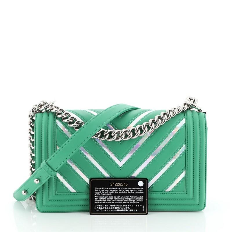 This Chanel Boy Flap Bag Chevron Lambskin with Holographic PVC Old Medium, crafted from green leather and metallic textile, features chain link strap with adjustable leather strap and silver-tone hardware. Its CC boy push-lock closure opens to a