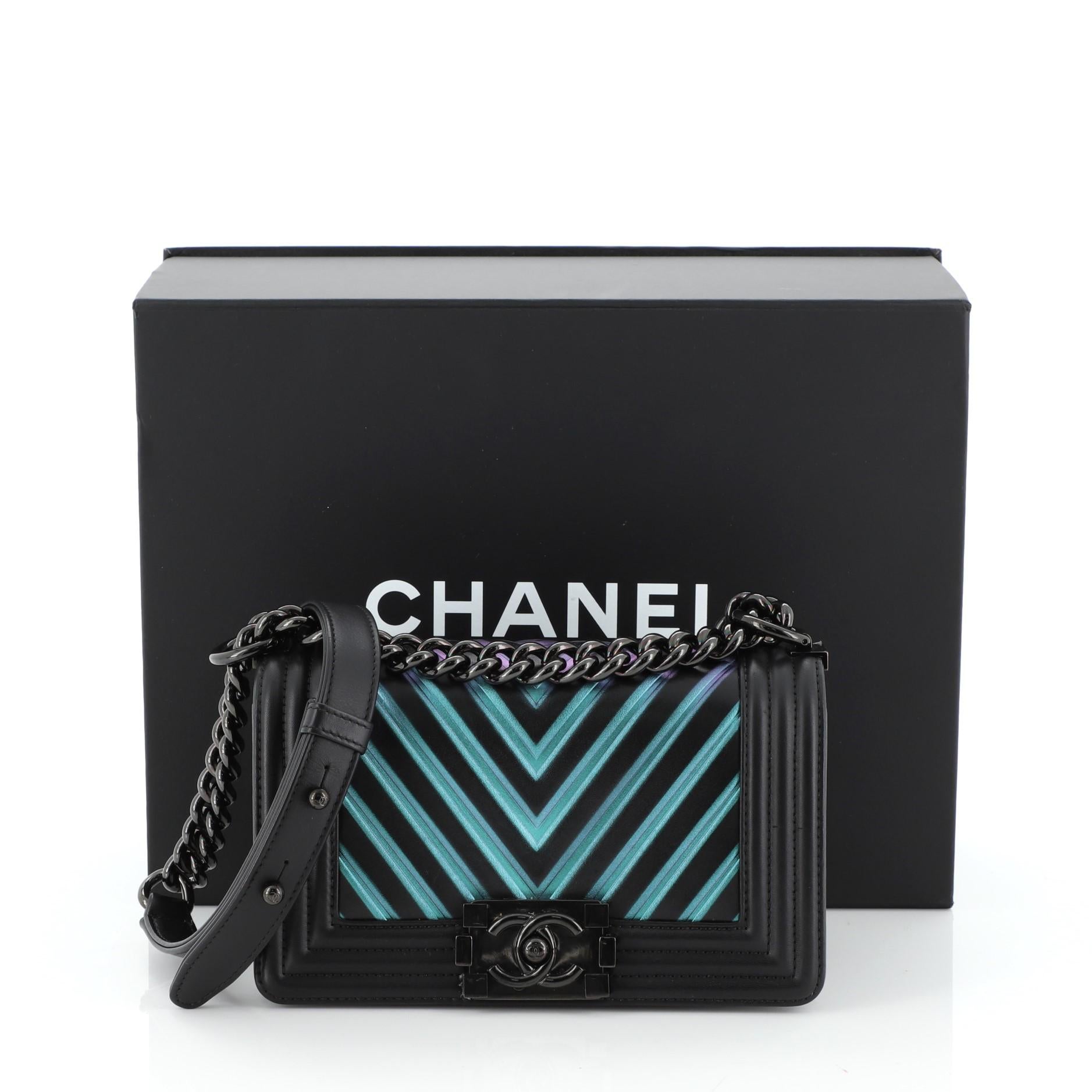 This Chanel Boy Flap Bag Chevron Painted Calfskin Small, crafted from black and multicolor chevron painted calfskin leather, features chain link strap with leather pad, and black and iridescent rainbow-tone hardware. Its CC Boy push lock closure