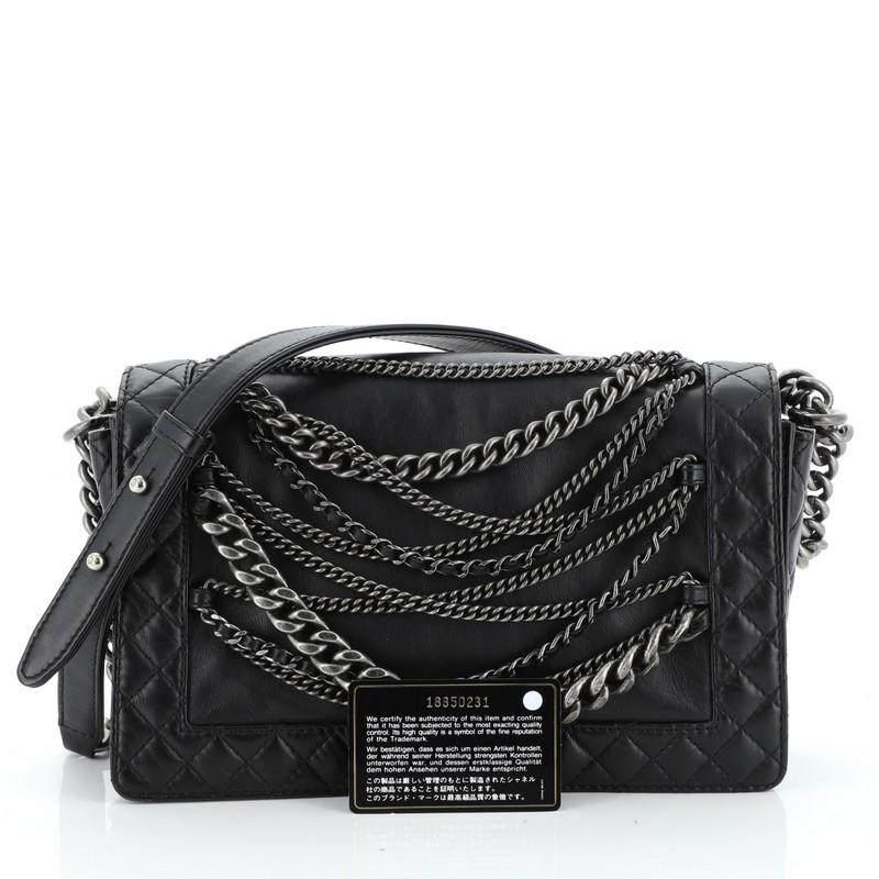 This Chanel Boy Flap Bag Enchained Lambskin New Medium, crafted in black lambskin, features a chain link strap with leather pad and aged silver-tone hardware. Its Boy push-lock closure opens to a black nylon interior with slip and zip pockets.