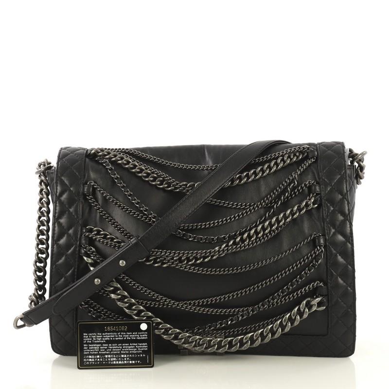 This Chanel Boy Flap Bag Enchained Lambskin XL, crafted in black lambskin leather, features chain link strap with leather pad, draped metal chains on front flap, and aged silver-tone hardware. Its boy push-lock closure opens to a black fabric