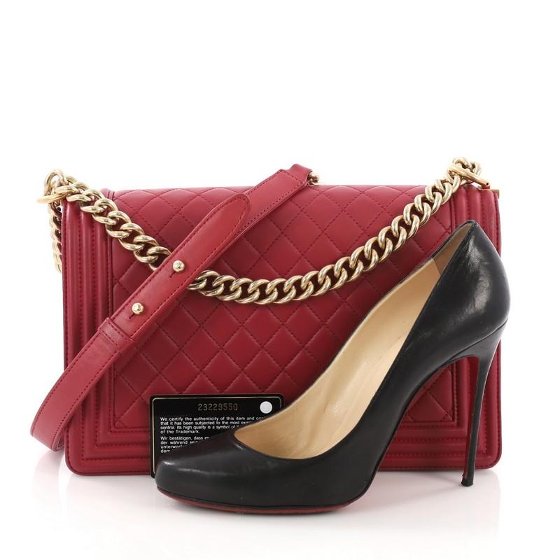 This Chanel Boy Flap Bag Quilted Lambskin New Medium, crafted from red quilted lambskin leather, features a chunky chain link strap with leather shoulder pad and aged gold-tone hardware. Its push-lock closure opens to a pink fabric interior with zip