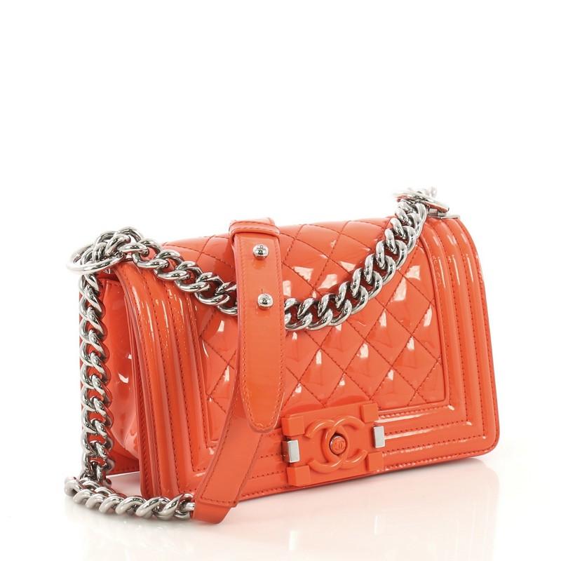 This Chanel Boy Flap Bag Quilted Plexiglass Patent Small, crafted from orange quilted plexiglass patent leather, features chain link strap with shoulder pad and silver-tone hardware. Its plexiglass CC Boy push-lock closure opens to a black fabric