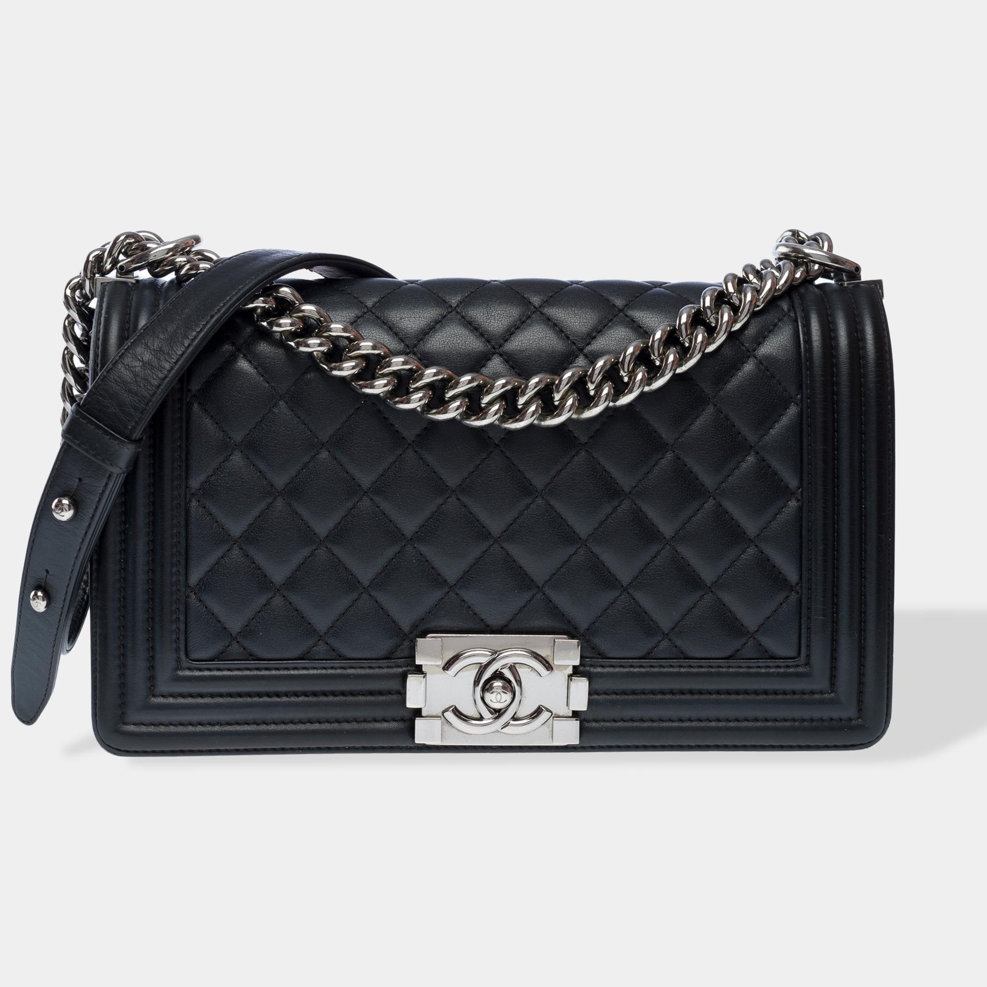 El icónico bolso Chanel Boy Old Medium de piel de cordero acolchada negra, con adornos metálicos plateados y una correa ajustable de cadena metálica plateada que permite llevarlo al hombro o cruzado.

Cierre con logotipo de metal plateado en la