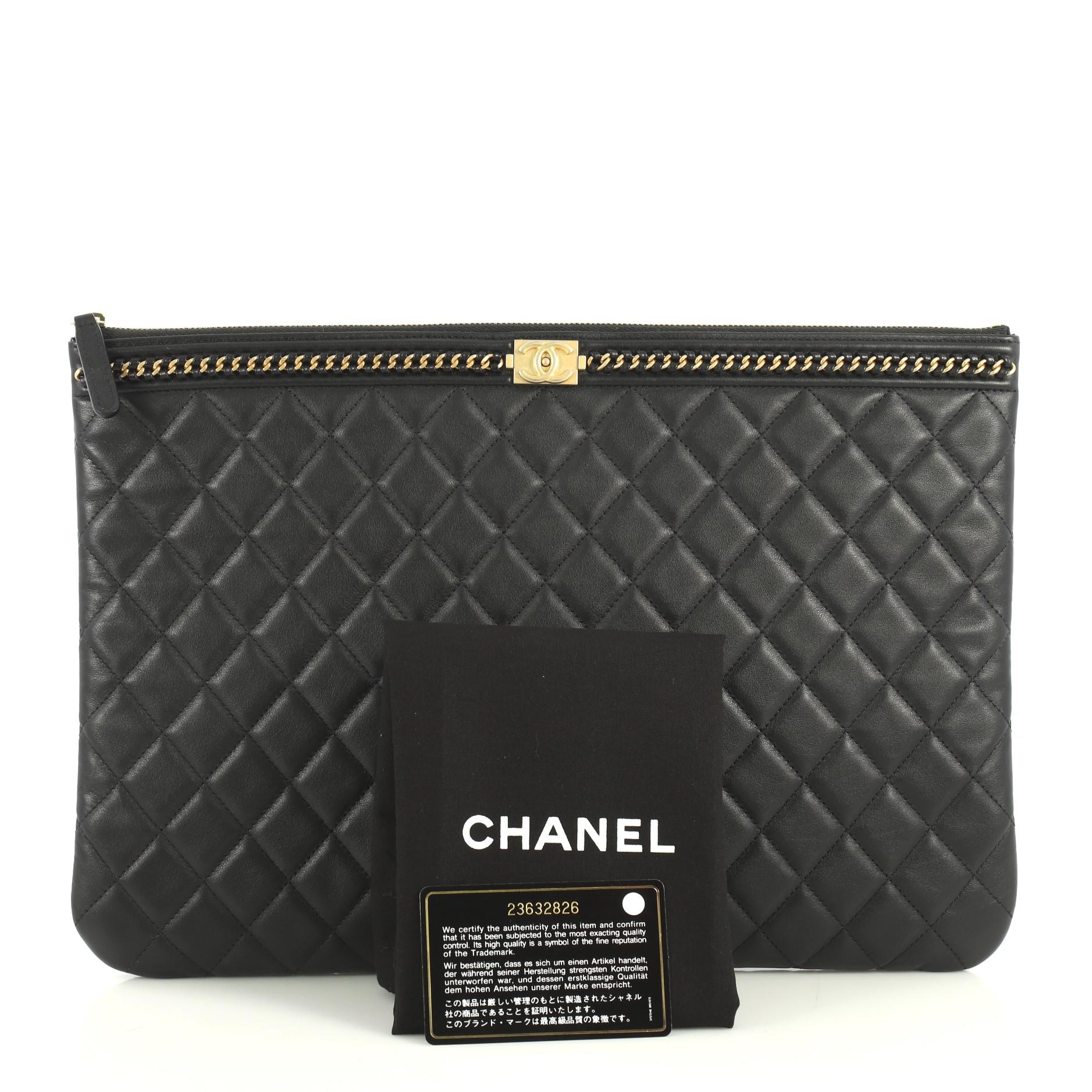 This Chanel Boy O Case Clutch Quilted Lambskin with Chain Detail Large, crafted from black quilted lambskin leather, features chain detail on top border, Chanel boy logo press lock, and gold-tone hardware. Its zip closure opens to a black nylon