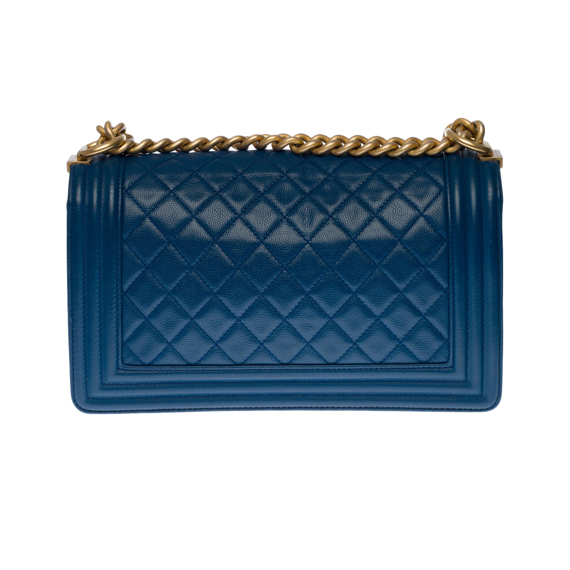 The iconic Chanel Boy Old Medium shoulder bag in blue quilted caviar leather with matte gold metal hardware, an adjustable chain handle in matte gold metal allowing a shoulder or shoulder strap.
A matte gold-tone metal logo closure on the