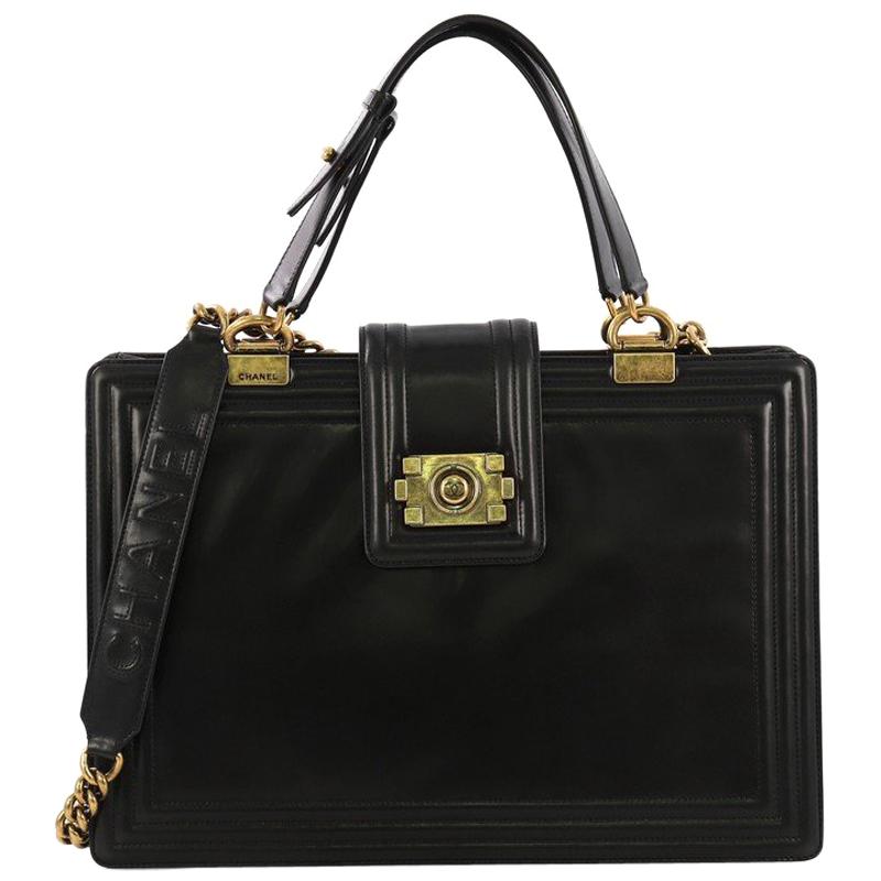 This Chanel Boy Tote Glazed Calfskin Large, crafted from black glazed calfskin leather, features dual flat leather handles, chain link strap with leather pad, quilted border and aged gold-tone hardware. Its boy push-lock closure opens to a black