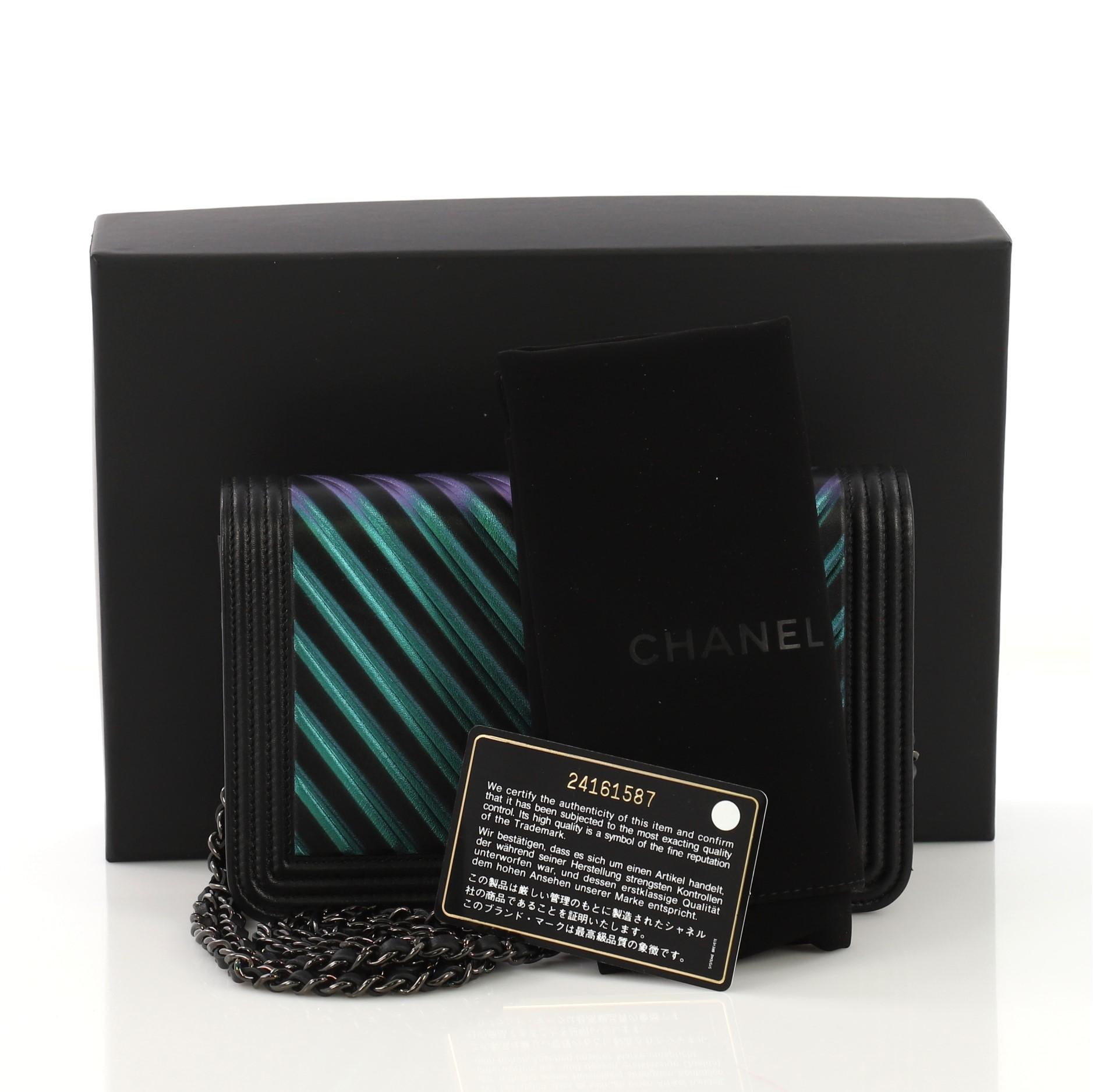 This Chanel Boy Wallet on Chain Chevron Painted Calfskin, crafted from black iridescent chevron painted calfskin leather, features woven-in leather chain strap, classic Chanel boy insignia, and black-tone hardware. Its hidden magnetic snap closure
