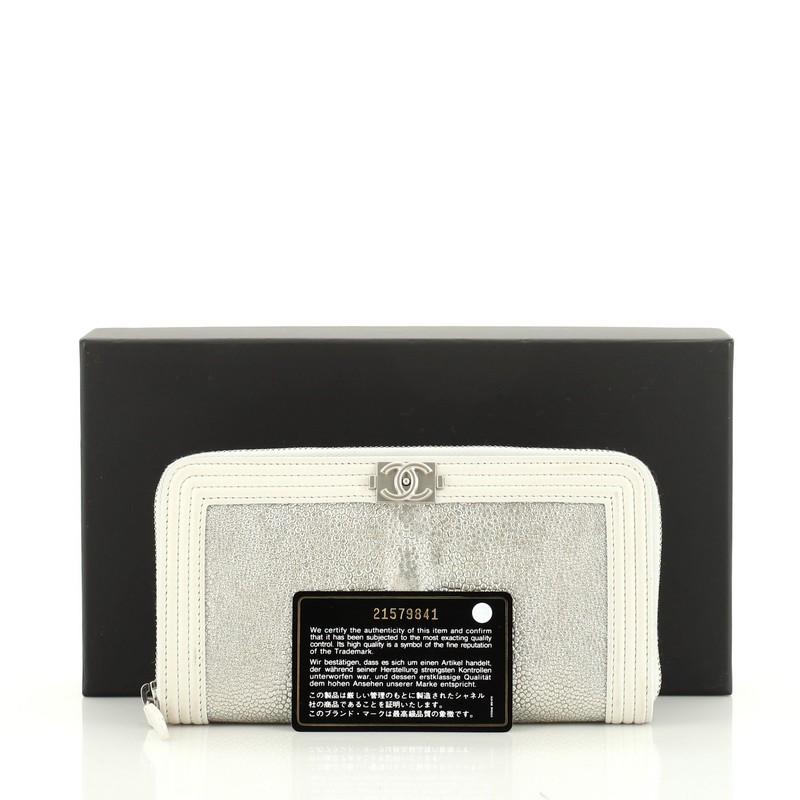 This Chanel Boy Zip Around Wallet Galuchat Long, crafted from genuine silver galuchat, features faux CC boy push-lock and silver-tone hardware. Its all-around zip closure opens to a blue leather and fabric interior with gusseted compartments, zip