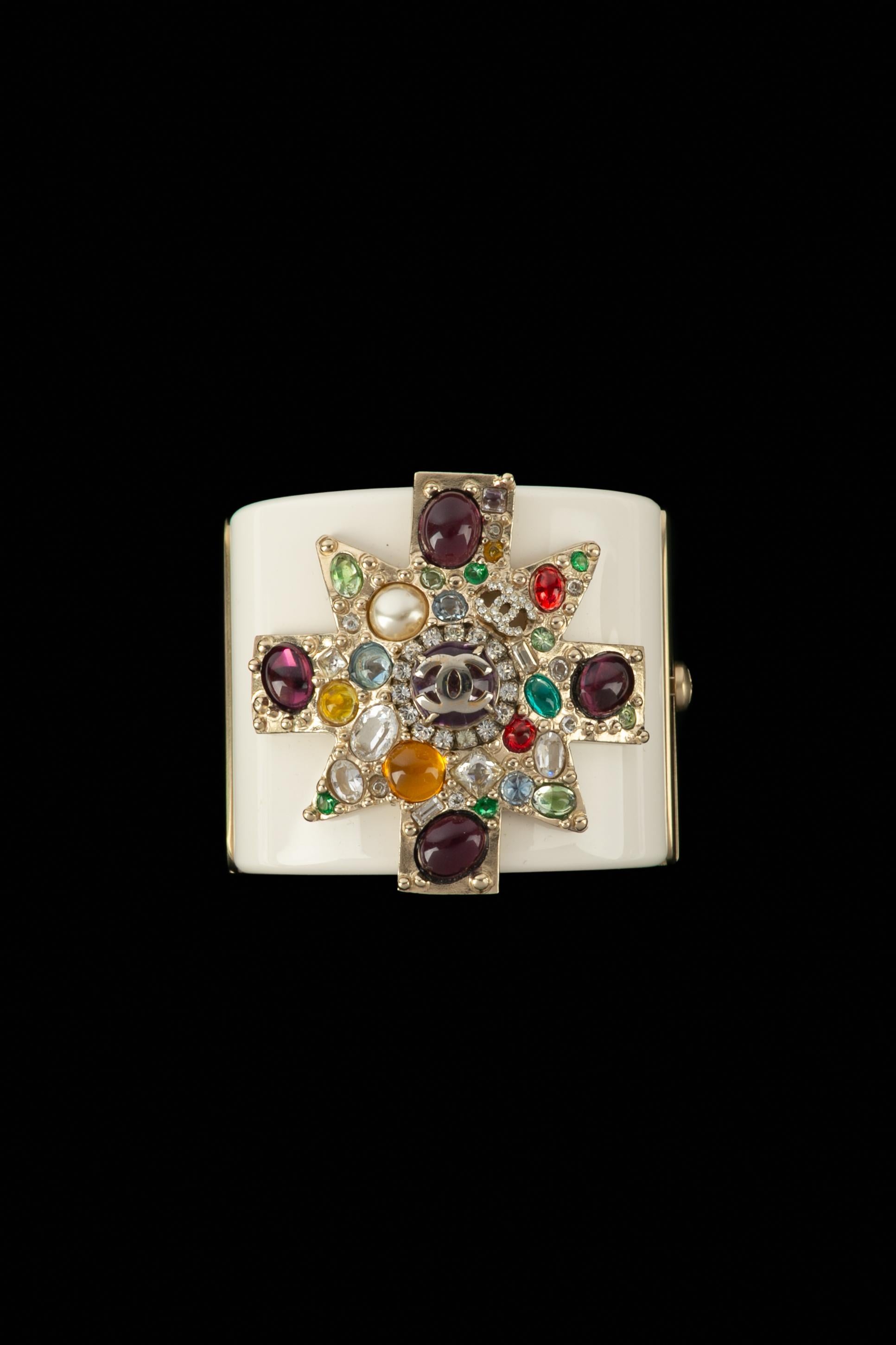 CHANEL - (Made in France) Manschettenarmband aus weißem Bakelit, verziert mit einem goldenen Metallkreuz und bunten Strasssteinen. A 2011 Collection'S.

Bedingung:
Sehr guter Zustand

Abmessungen:
Umfang: 17 cm - Höhe: 5 cm

SKU:BRAB109