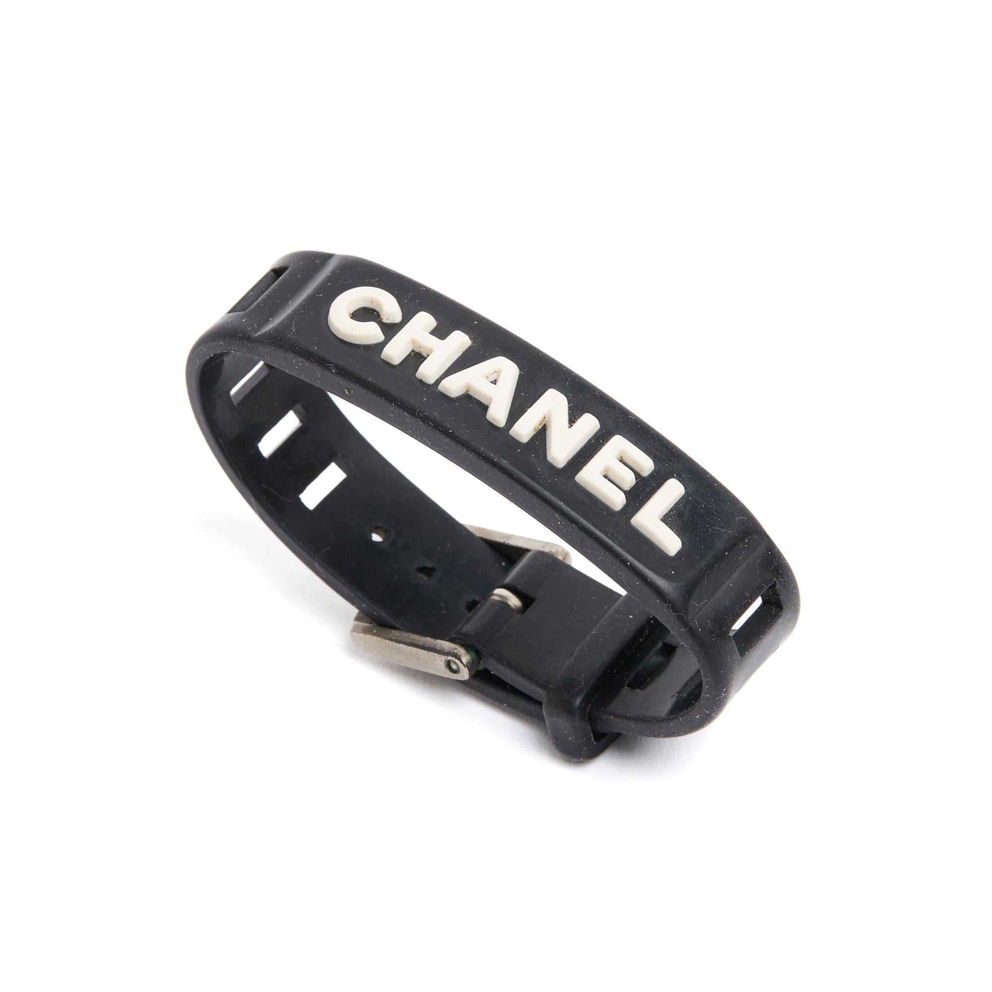 Bracciale Chanel collezione SS1999 in caucciù nero e logo CHANEL bianco, chiusura regolabile con fibbia in metallo argentato, firmato. Larghezza del bracciale 1,6 cm, lunghezza totale del bracciale 21,5 cm, chiusura da 16,5 a 19,5 cm su 5 fori. Il