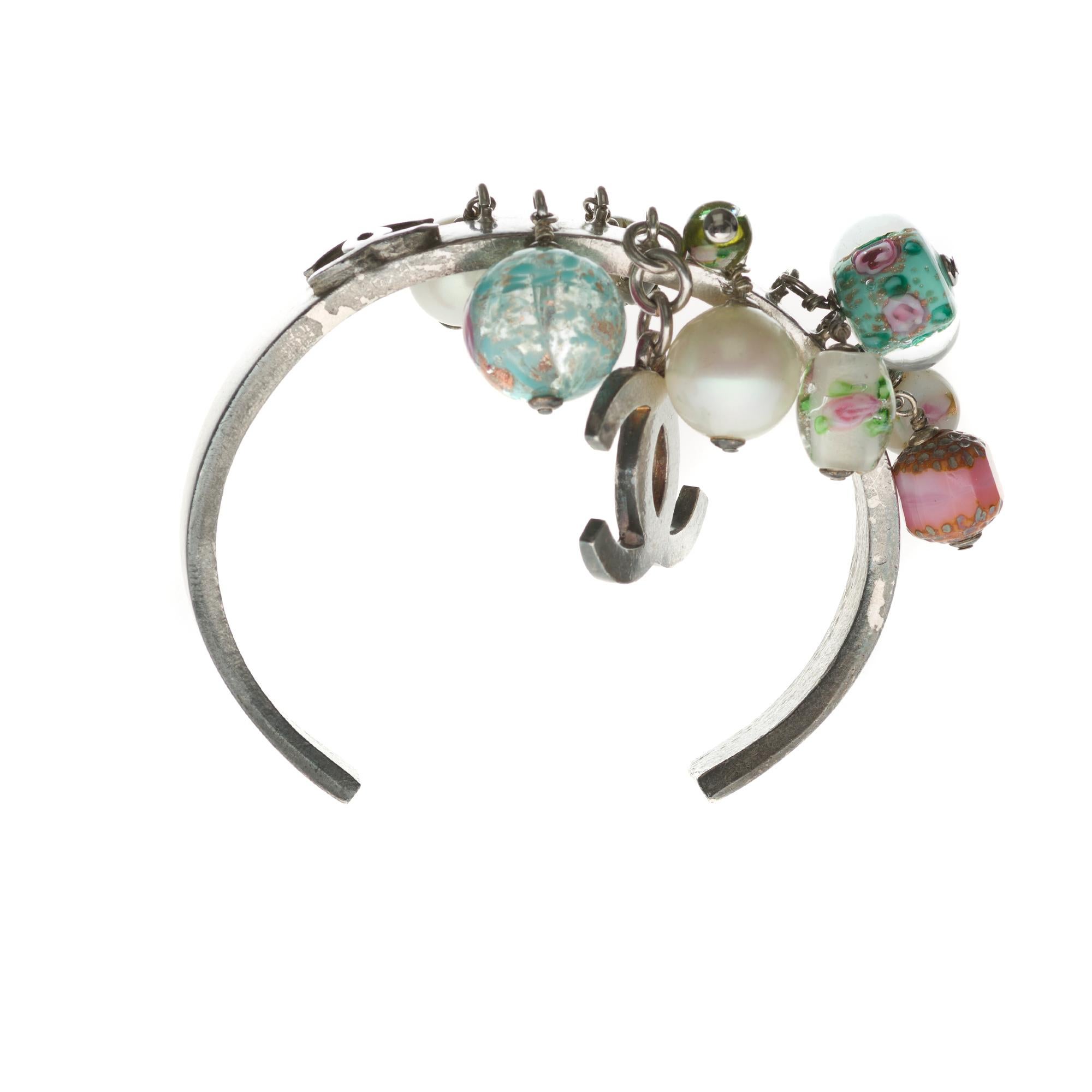 Silver metal cuff bracelet with charms in multicoloured pearls and fancy stones, matched with a silver metal CC.
Strap width in the middle: 6cm.
Width base cuff: 3cm

In good general condition despite signs of wear on metal and charms.