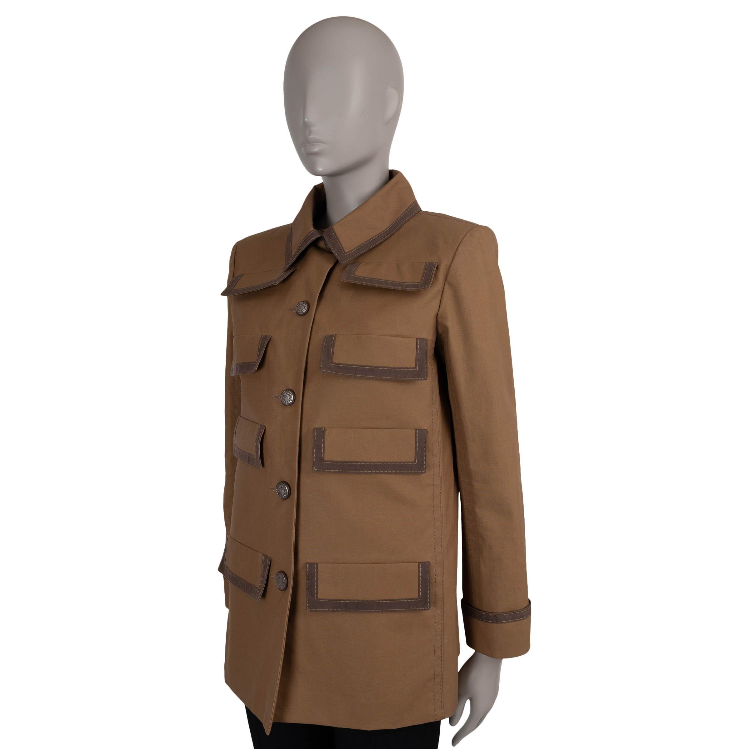 Questa giacca Chanel autentica al 100% in gabardine di cotone marrone bronzo (100%) con finiture marrone scuro è un pezzo raffinato con un tocco di ispirazione safari. Progettato con una silhouette sartoriale e leggermente allungata, presenta otto