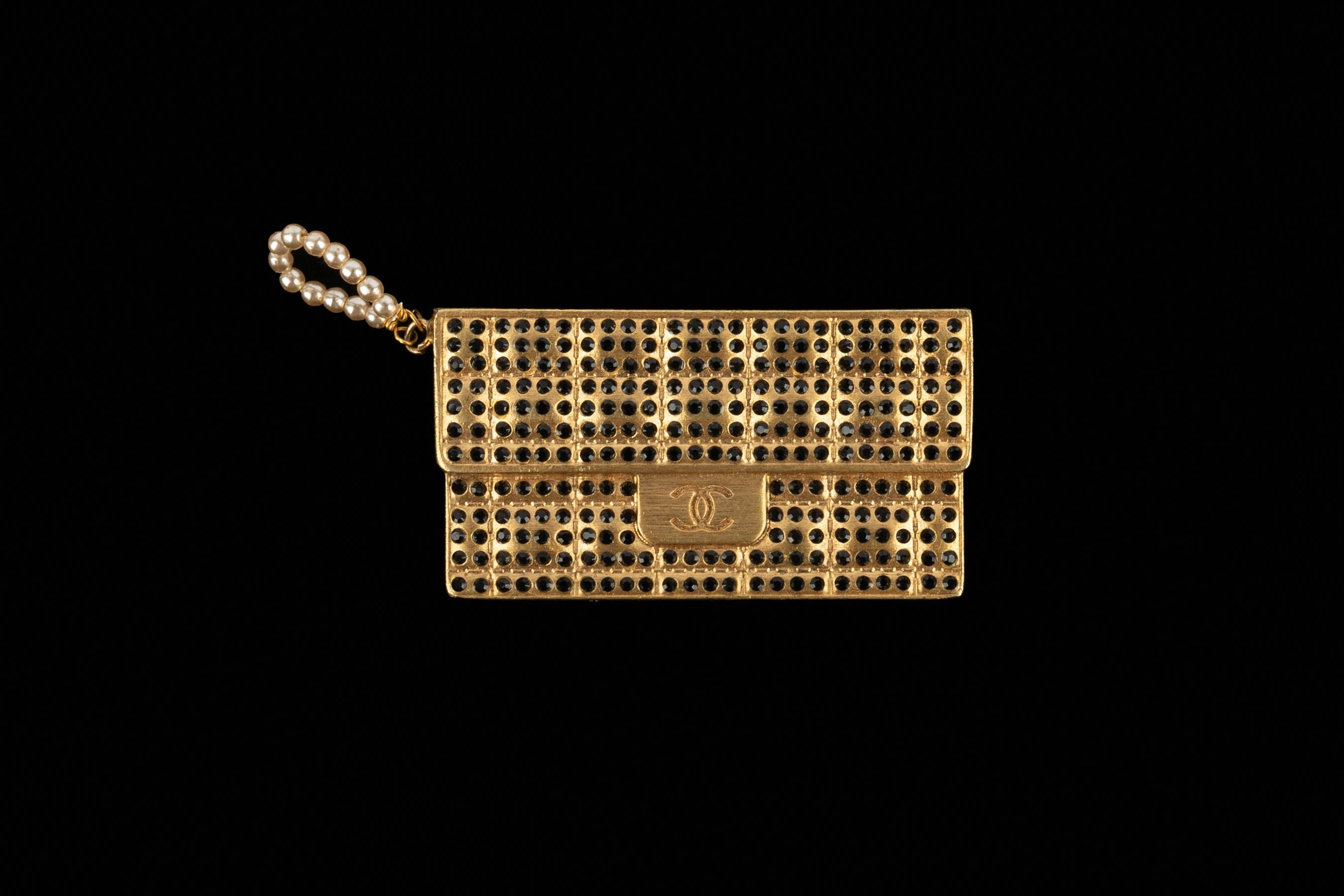 CHANEL - (Fabricado en Francia) Broche de metal dorado que representa un bolso Chanel adornado con brillantes Swarovski negros. Pequeña asa de perlas de fantasía. Colección Otoño-Invierno 2002 bajo la dirección artística de Karl