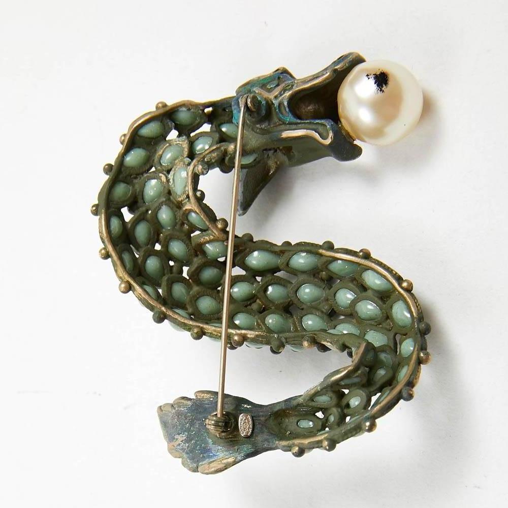 Exquisite Chanel Brooch in green color molten glass. The dragon has in its mouse a faux pearl. An iconic CC symbol is engraved at the end of the dragon's tail. The brooch is in very good condition. Made in France in 2009. Mesures: 7.5 cm height x 5
