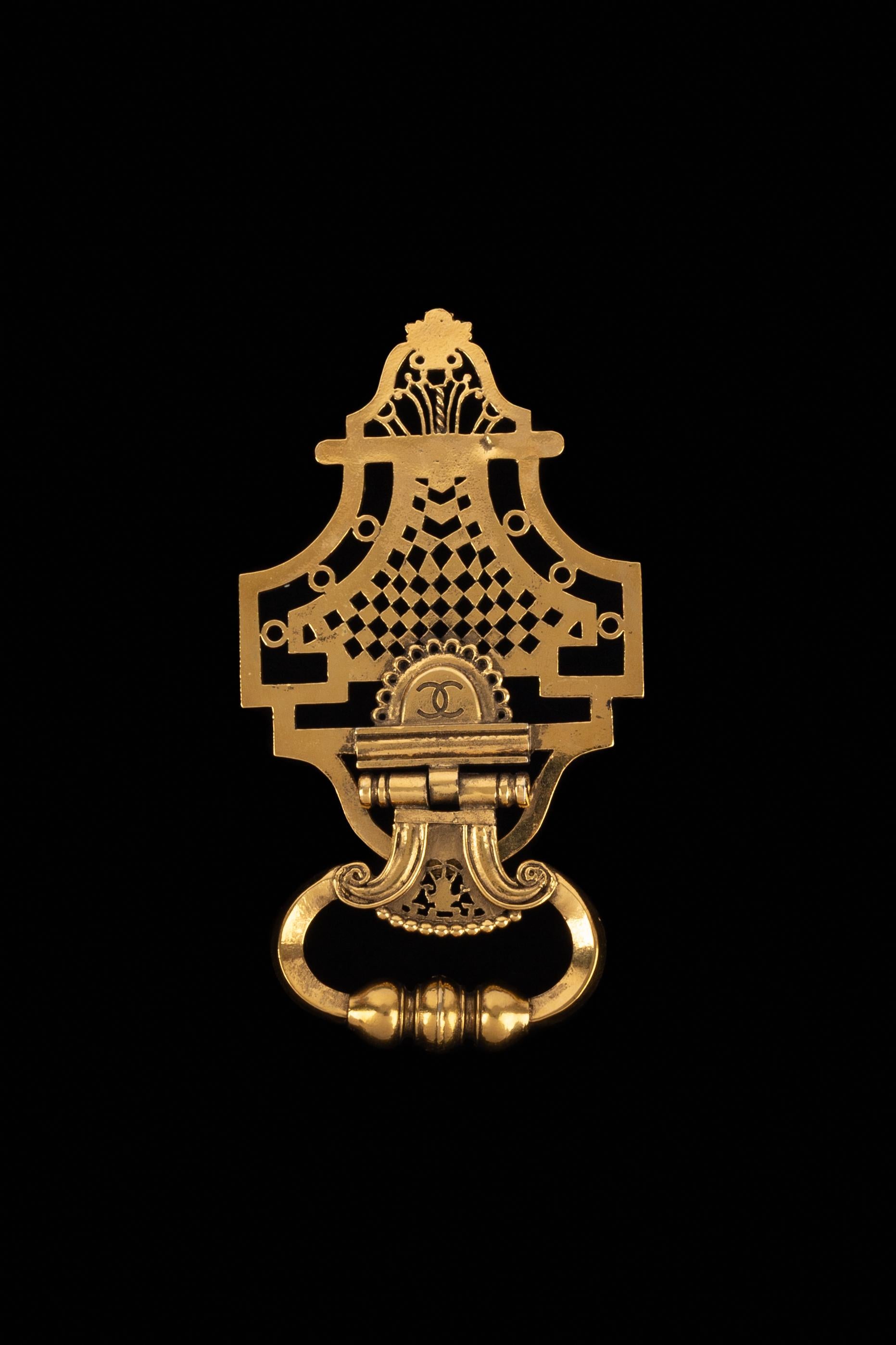 CHANEL - Broche en métal doré ajouré représentant un heurtoir. Collectional automne-hiver 1989, sous la direction artistique de Karl Lagerfeld.

Condit :
Très bon état.

Dimensions :
14 cm x 7.5 cm

SKU:BRB56