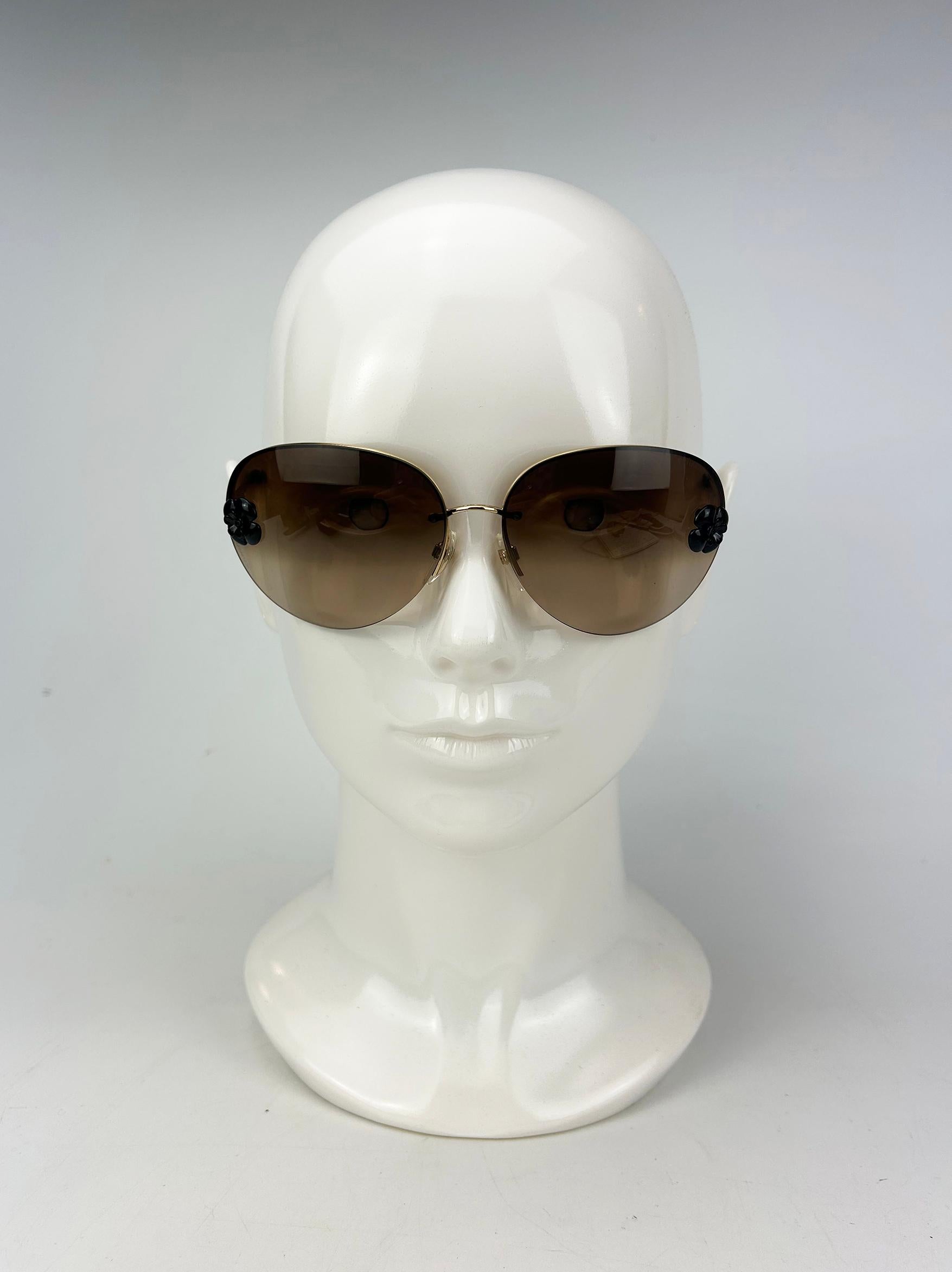 Chanel Brown Frameless Aviator Sunglasses with Black Flower in very good condition. Brown gradient tint lenses with gold tone hardware frame and delicate black acrylic camellia flower on each side of lens. Frameless style appears as though the
