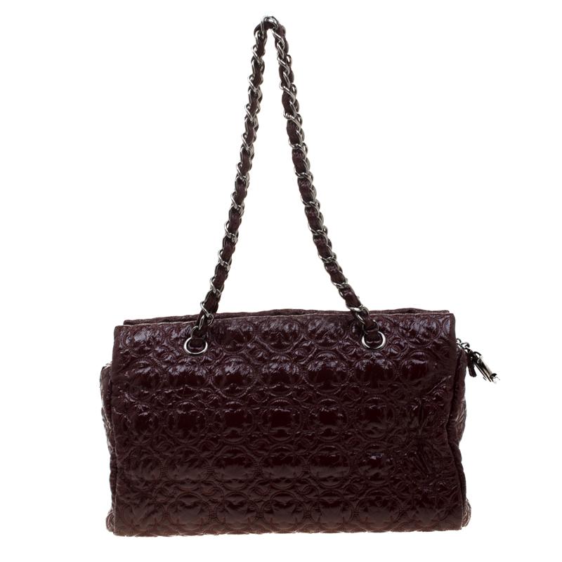 This bag from Chanel is a beautiful handbag dream. It comes crafted from burgundy patent leather and is held by chains. The exterior of the bag has stitches in camellia patterns and the top leads way to a satin interior housing the brand label and