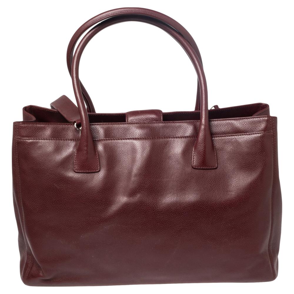 This Cerf tote from Chanel is a perfect blend of function and style. It features a burgundy leather construction that is enhanced with a silver-tone CC logo on the front and dual top handles. It is equipped with a spacious interior that can easily