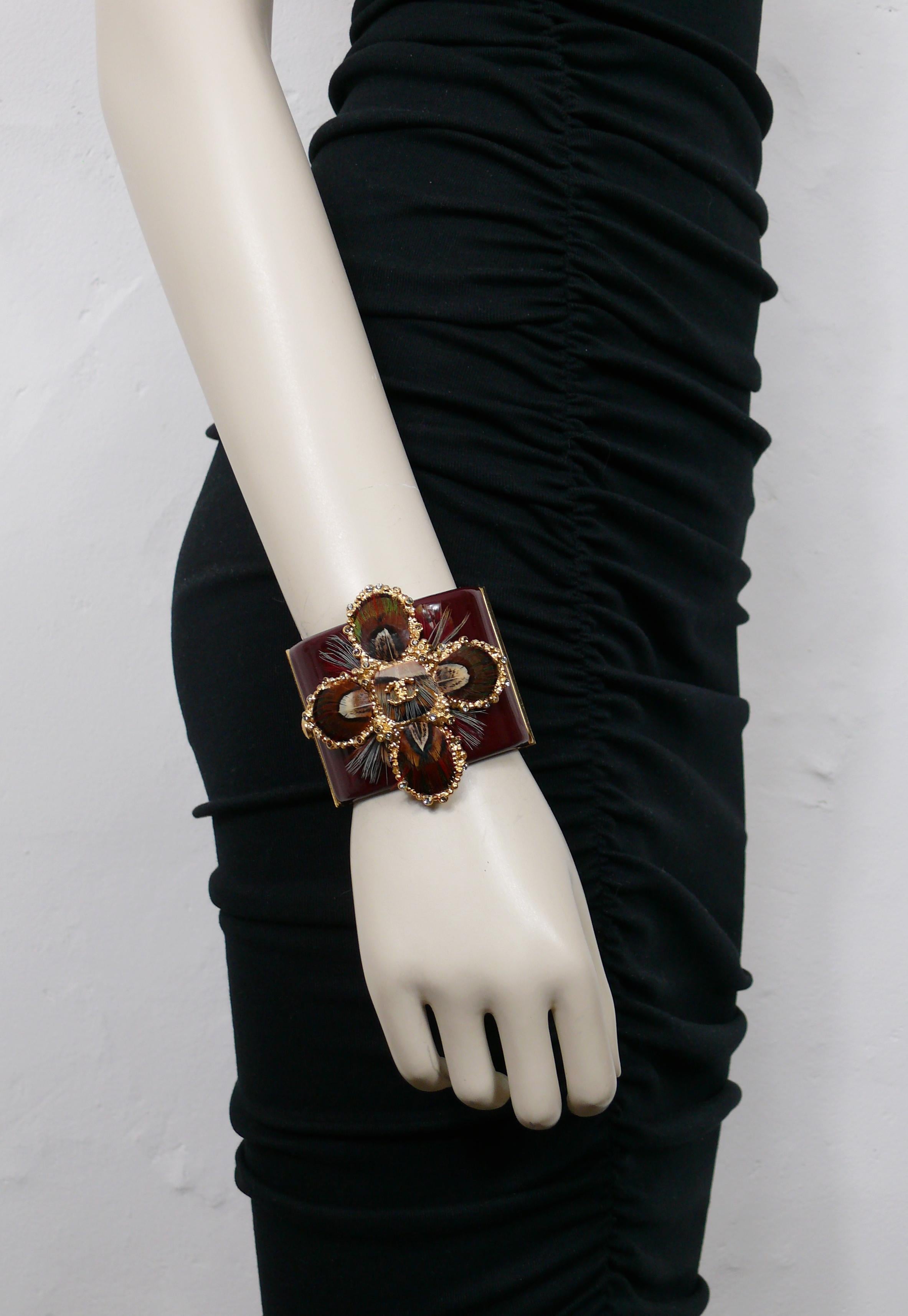 CHANEL by KARL LAGERFELD burgundy resin cuff bracelet featuring a gorgeous textured gold toned cross embellished with multicolored crystals, feathers and a CC logo at the center.

From the Pre-Fall 2013 Metiers D'Art Paris-Edinburgh