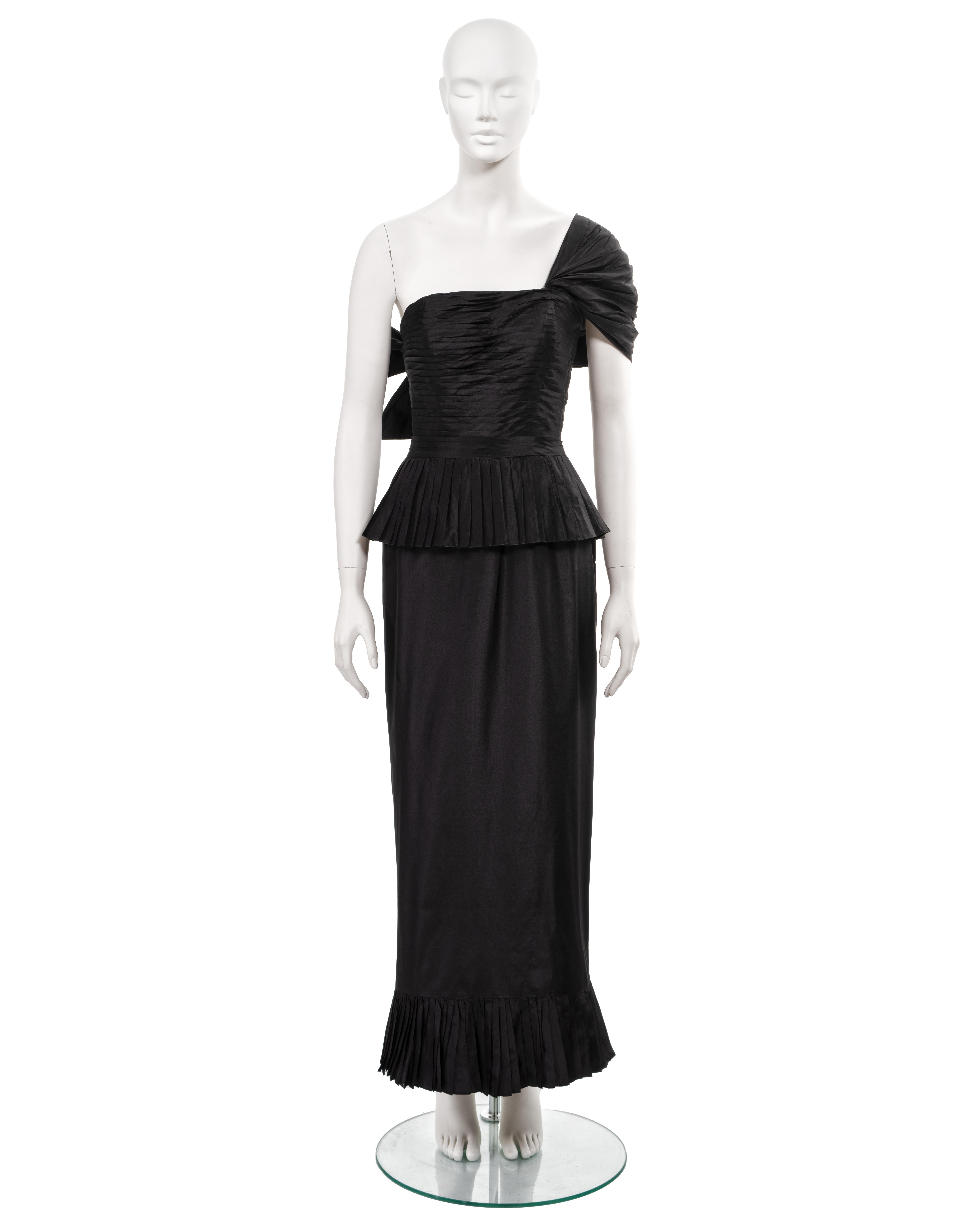 ▪ Chanel evening dress
▪ Creative Director: Karl Lagerfeld 
▪ Sold by One of a Kind Archive
▪ Spring-Summer 1986
▪ Constructed from black silk taffeta 
▪ Fitted bodice with horizontal pleats 
▪ Asymmetric draped shoulder strap finishing with a bow