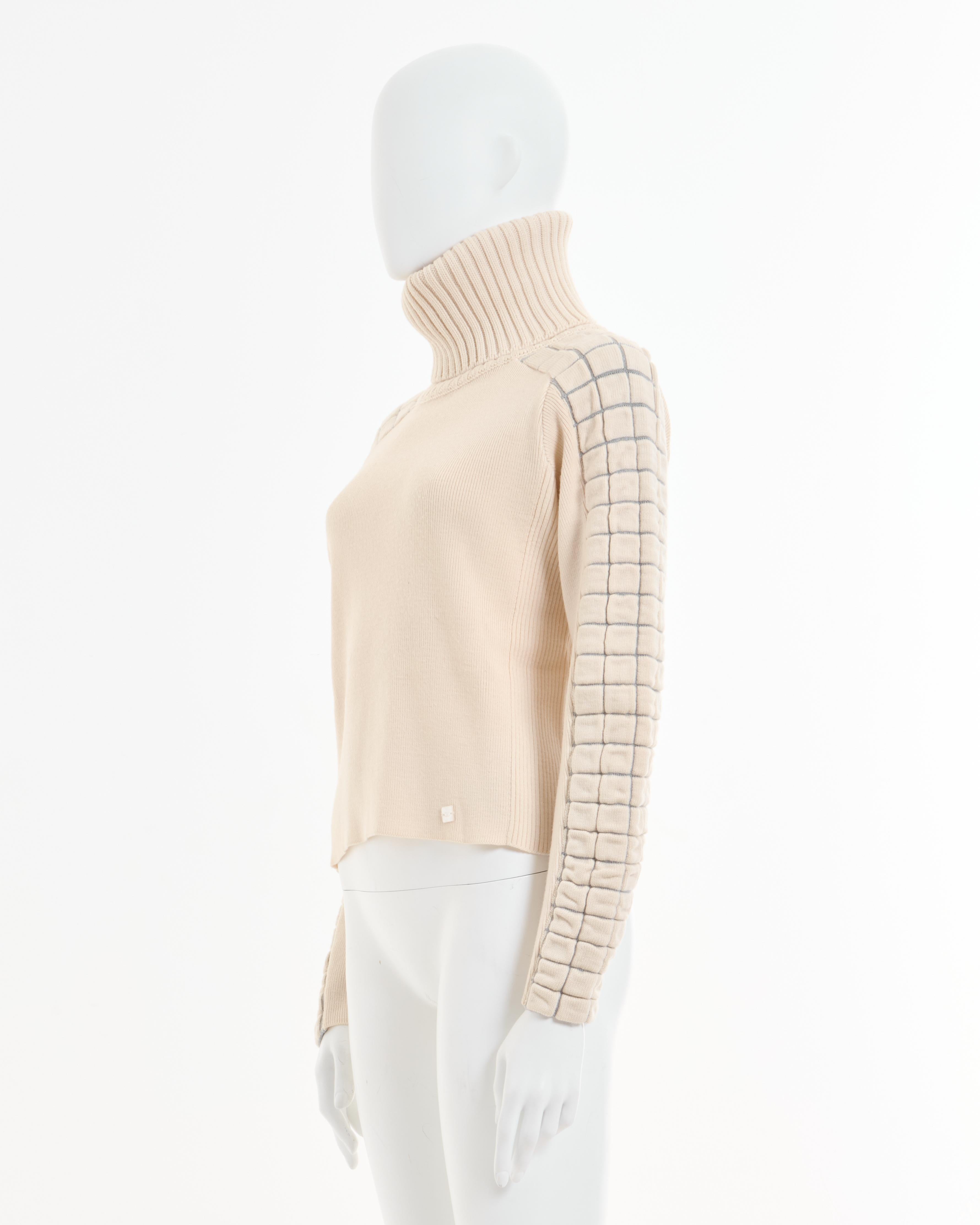 - Chanel gestrickter weißer Rollkragenpullover aus Wolle 
- Verkauft von Skof.Archive
- Entworfen von Karl Lagerfeld 
- Herbst-Winter 2002 
- Laufsteg-Look 23 und 27 
- Angepasst an den Körper 
- Schultern und Ärmel sind mit einem grauen Muster