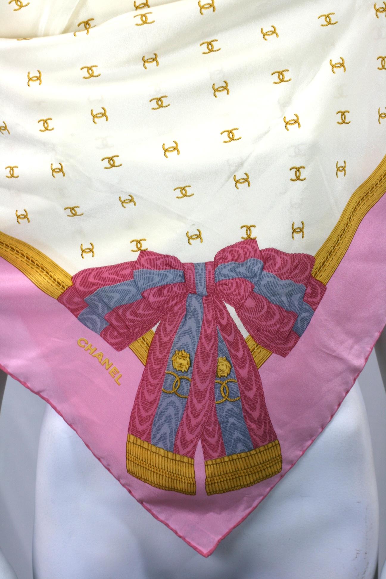 Chanel silk crepe de chine square scarf designed by Karl Lagerfeld. On a cream silk ground printed with gilt signature overlapping CCs with an old rose pink border.  A gilt braid inner border and an 18th century moire  large bow is  decorated with