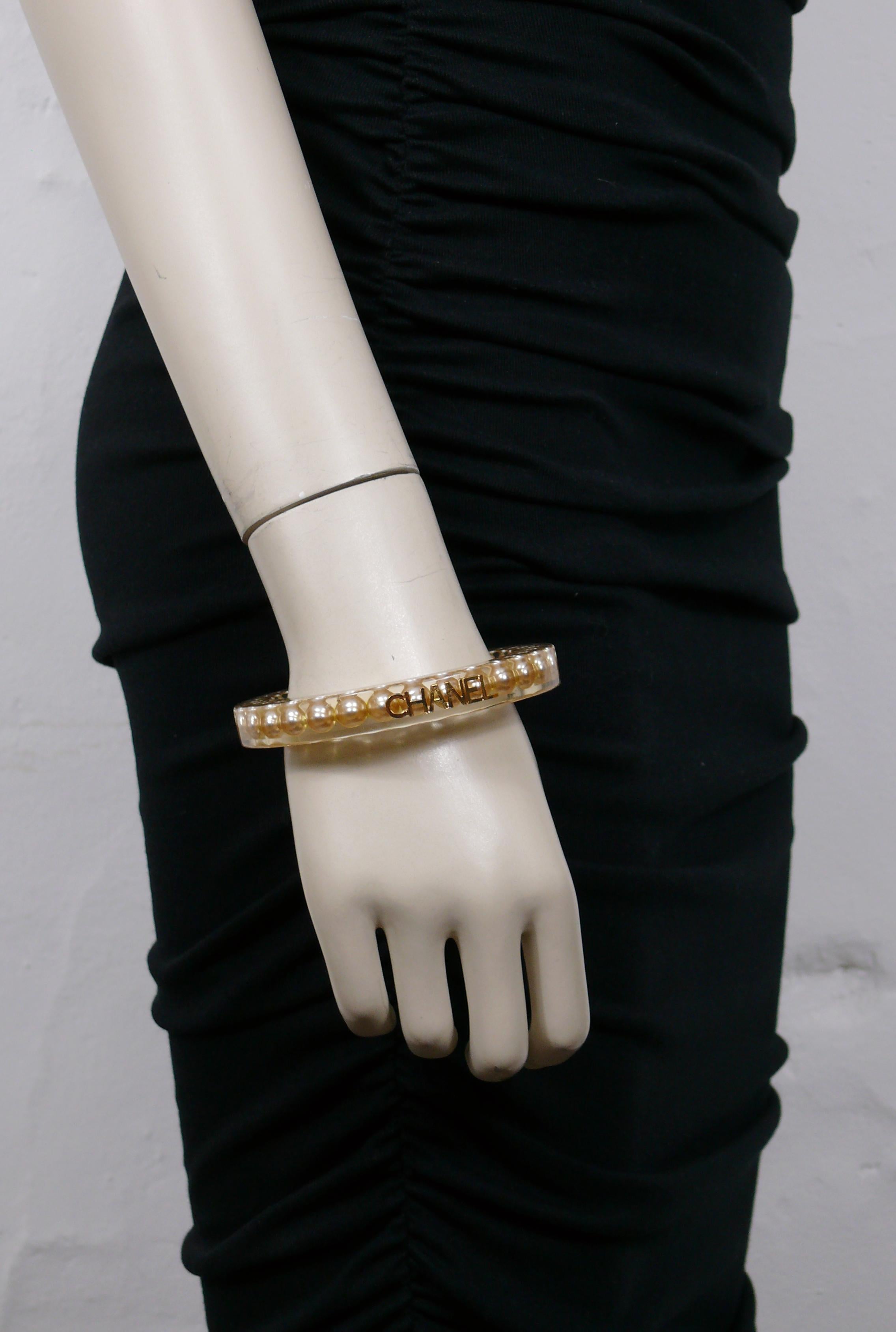 CHANEL by KARL LAGERFELD vintage lucite bangle bracelet embellished with faux pearl inlaid and gold tone CHANEL logo.

Spring collection 1997.

Embossed CHANEL 97 P Made in France.

Indicative measurements : inner circumference approx. 20.74 cm