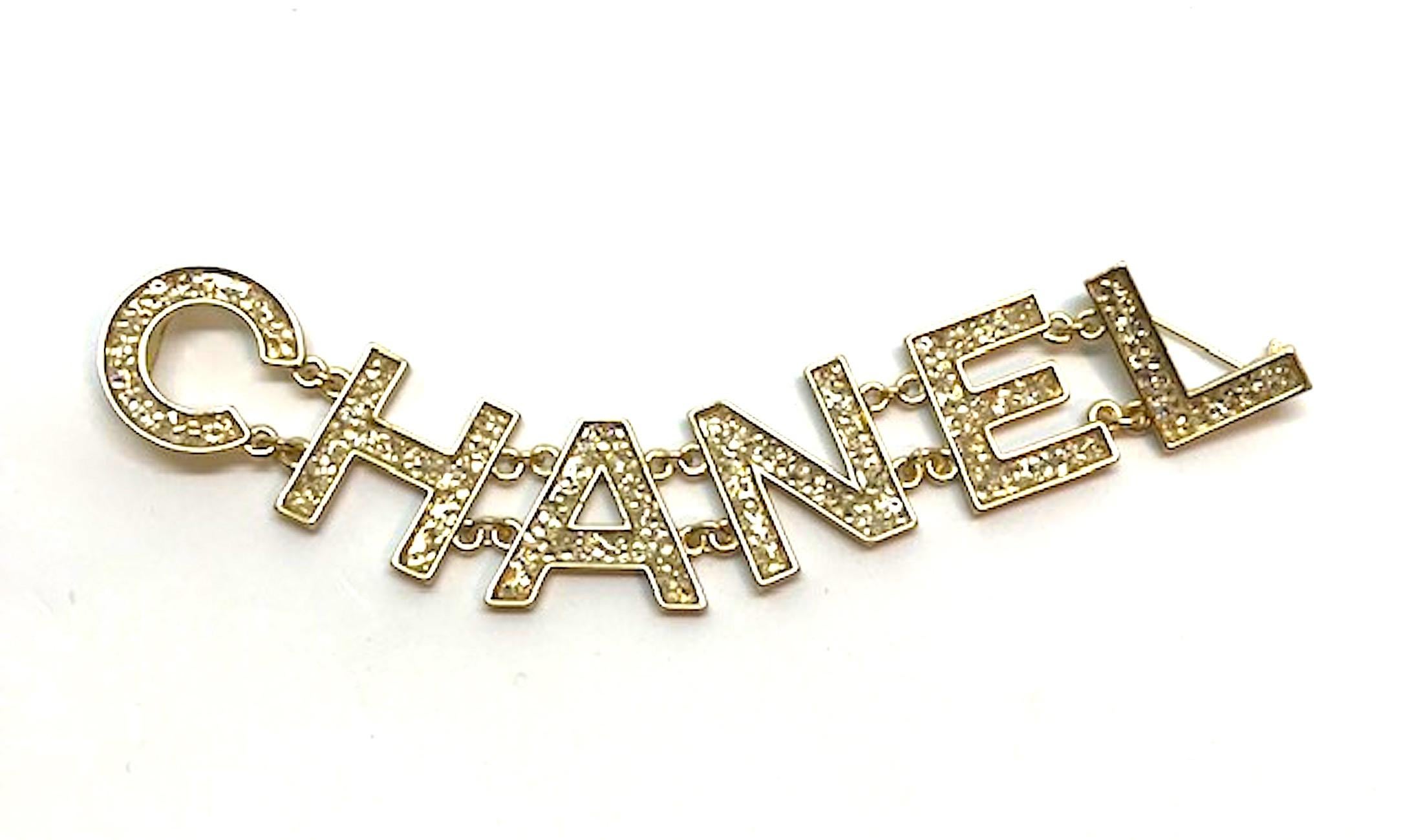 Chanel 2018 name in large pave' crystals and gold letters. Each letter is connected to the next with two sets of small links. Gold plate body. Each letter is filled with flat back mini crystals in a pave' style. Two pin backings. One on the 