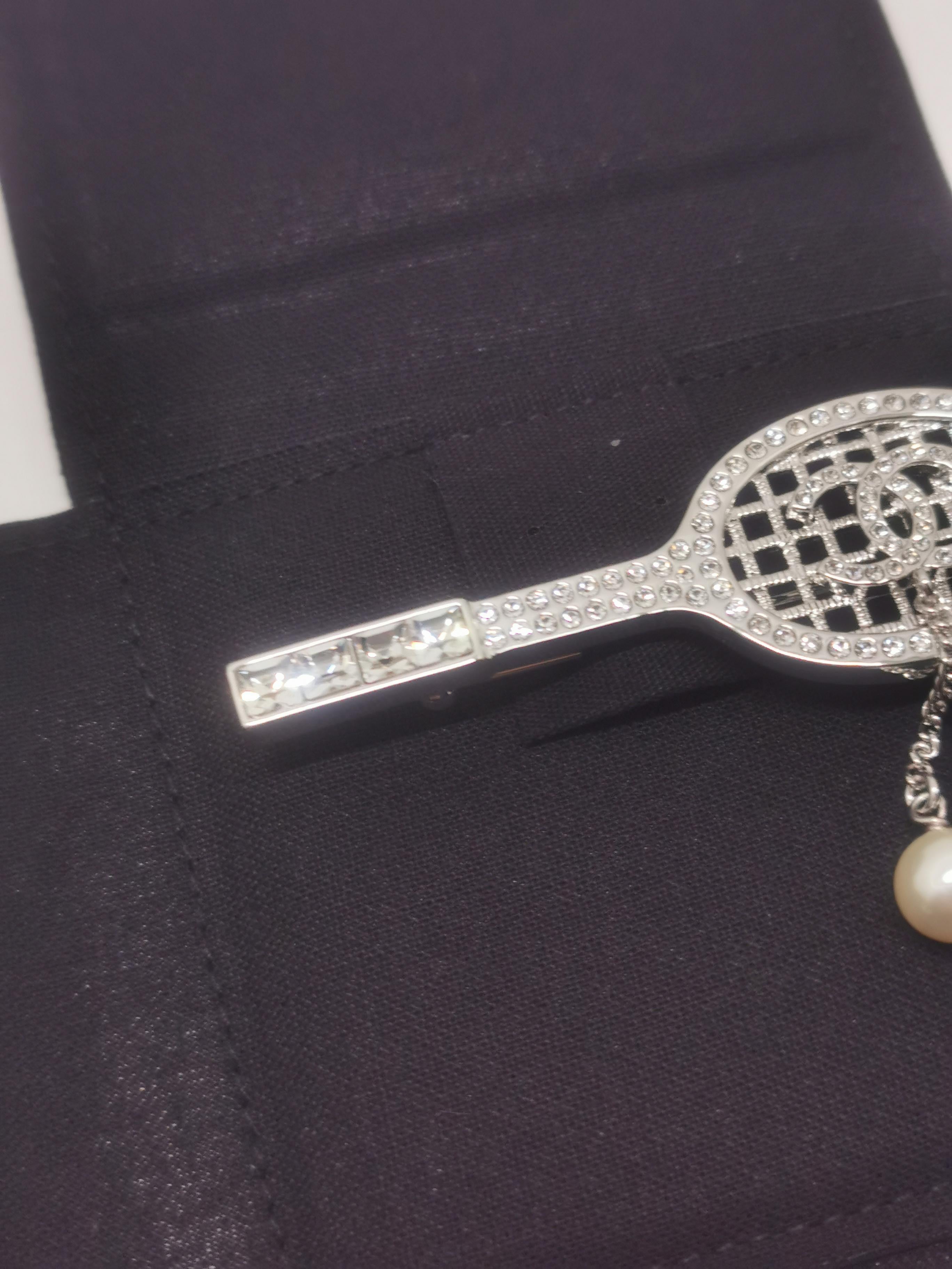 The Chanel B18 Tennis Racket Rhinestone CC Brooch is a distinctive and collectible piece from Chanel’s 2018 collection. This brooch features a tennis racket design adorned with rhinestones and the iconic interlocking CC logo. It's a rare item that