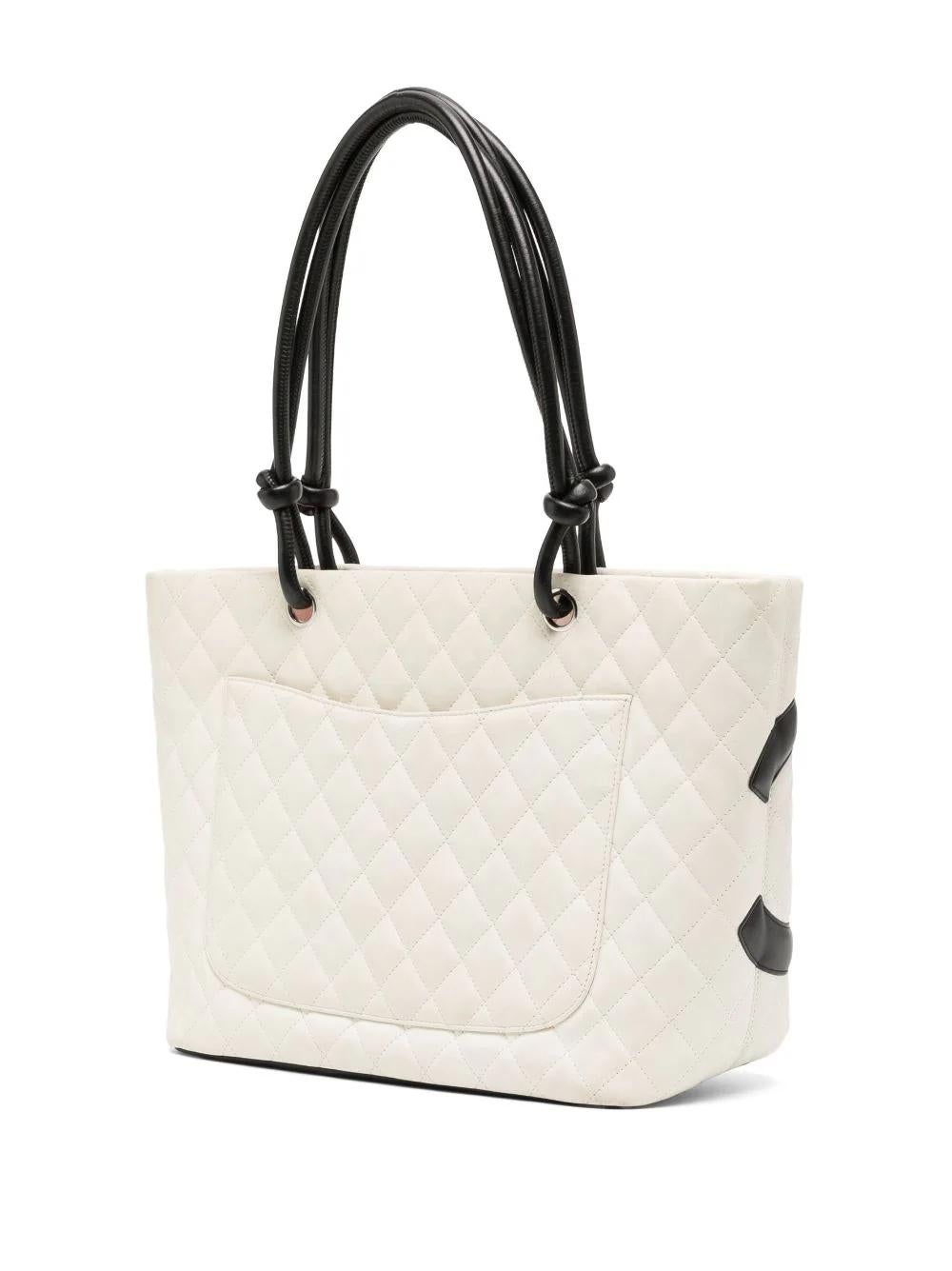 Crafted from a combination of white and black calfskin leather, this Chanel Quilted Tote features diamond quilting, a black logo patch, two leather straps, a top zip-fastening in bright pink that matches the interior lining and an internal
