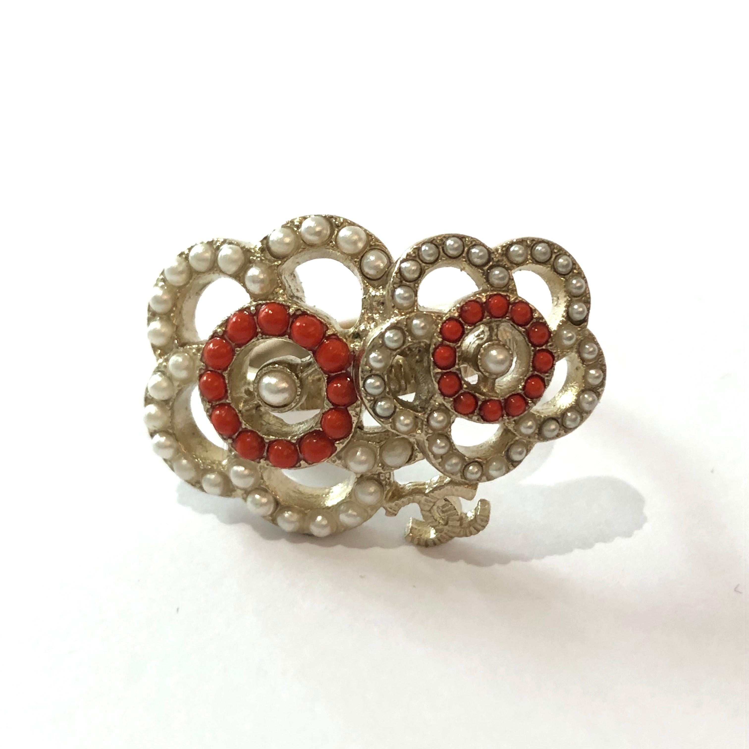 Iconic of the brand, this double camelia ring from Maison CHANEL is made of pale gold tone metal adorned with 2 camelia and the CC symbol. Each camelia are composed of small pearls in pearl and corail color. The ring is in perfect condition. It is