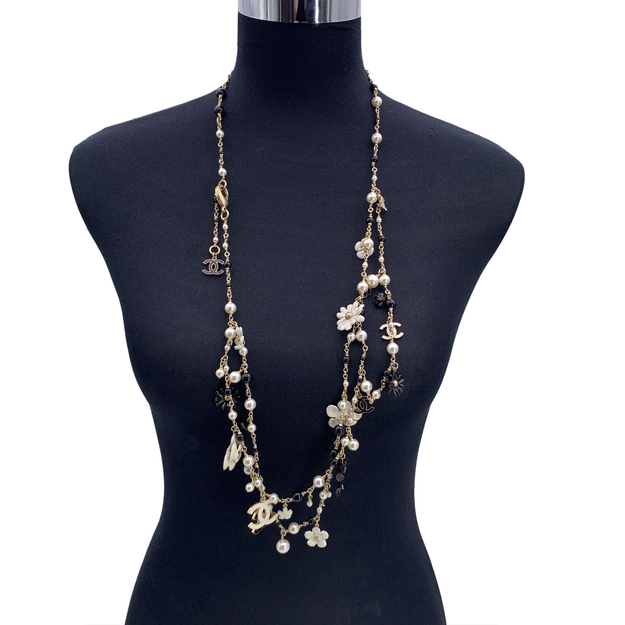 Long light gold metal multi strand chain necklace by Chanel. Light gold metal chain necklace by Chanel, from the Spring 2010. It features black beads, faux pearl beads, enameled black and white Camellia and daisy flowers with CC logos. Lobster