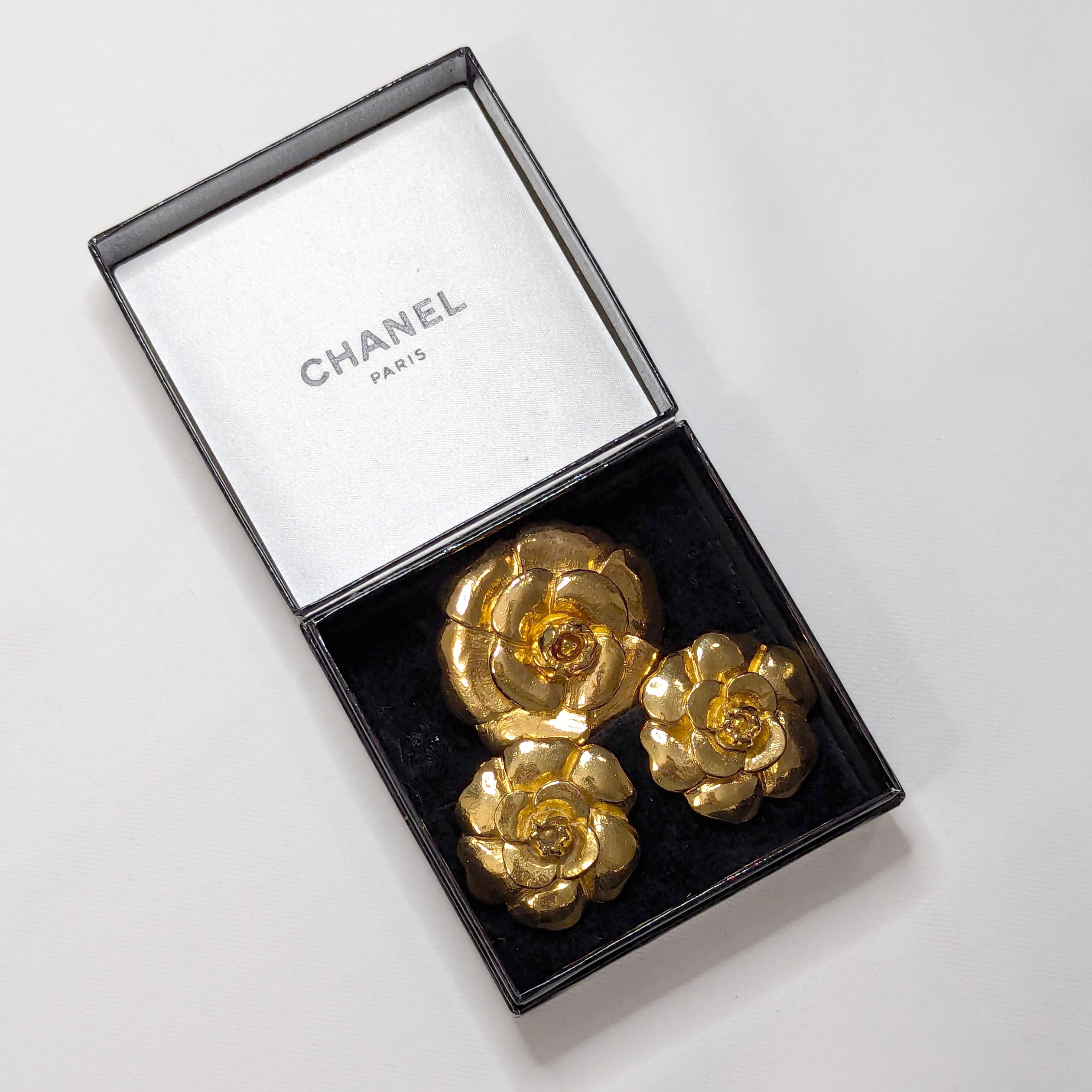 An exquisite Chanel Camelia gold tone flower brooch and a matching pair of earrings set, in a rich high-gloss finish. Camelia flowers have layers of petals in thick gold tone plating. Brooch has a single pin closure & safety lock, earrings are